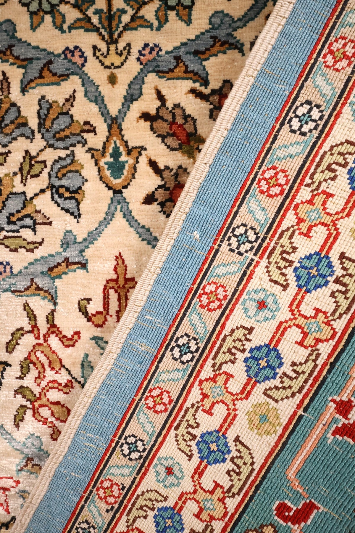 Coin replié du tapis Hereke en soie, passage du champ beige à la bordure