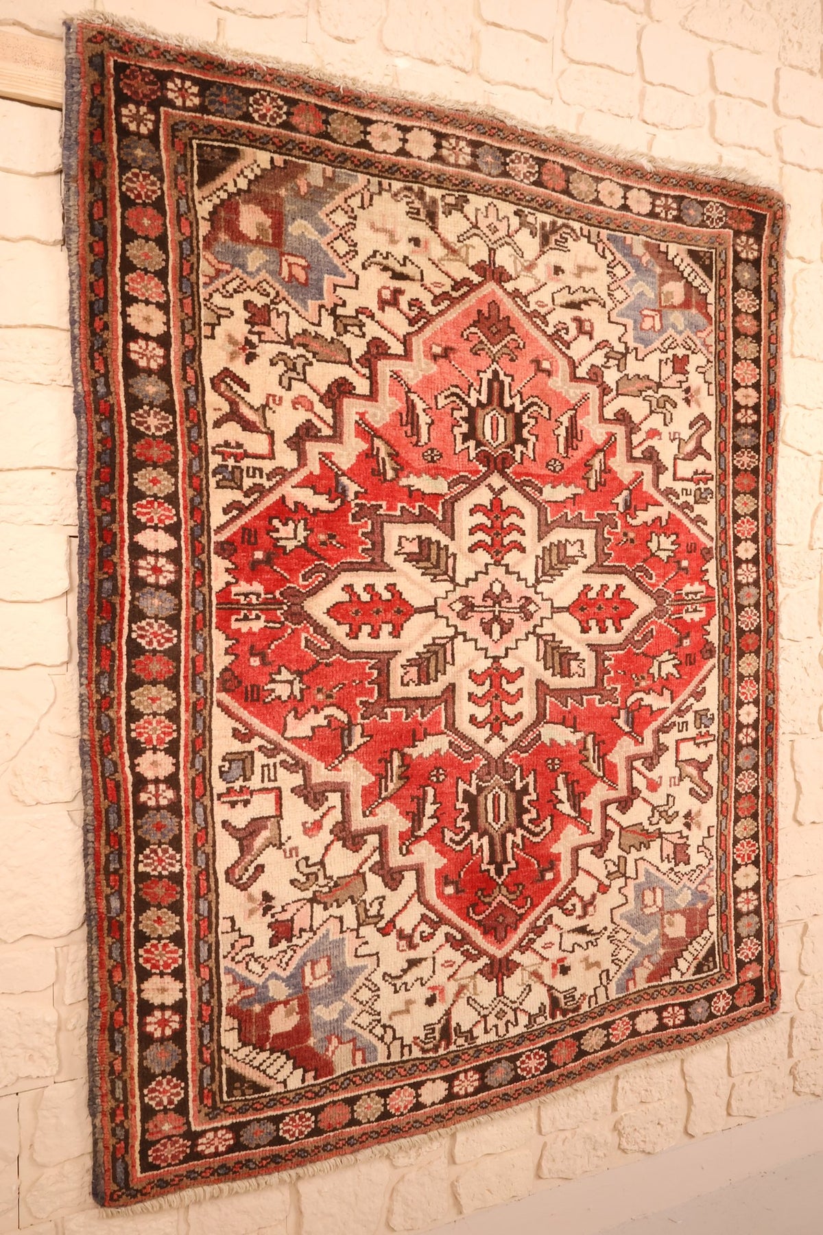 Tapis Heriz rouge et beige en laine, vue de biais sur le champ et les écoinçons ivoire