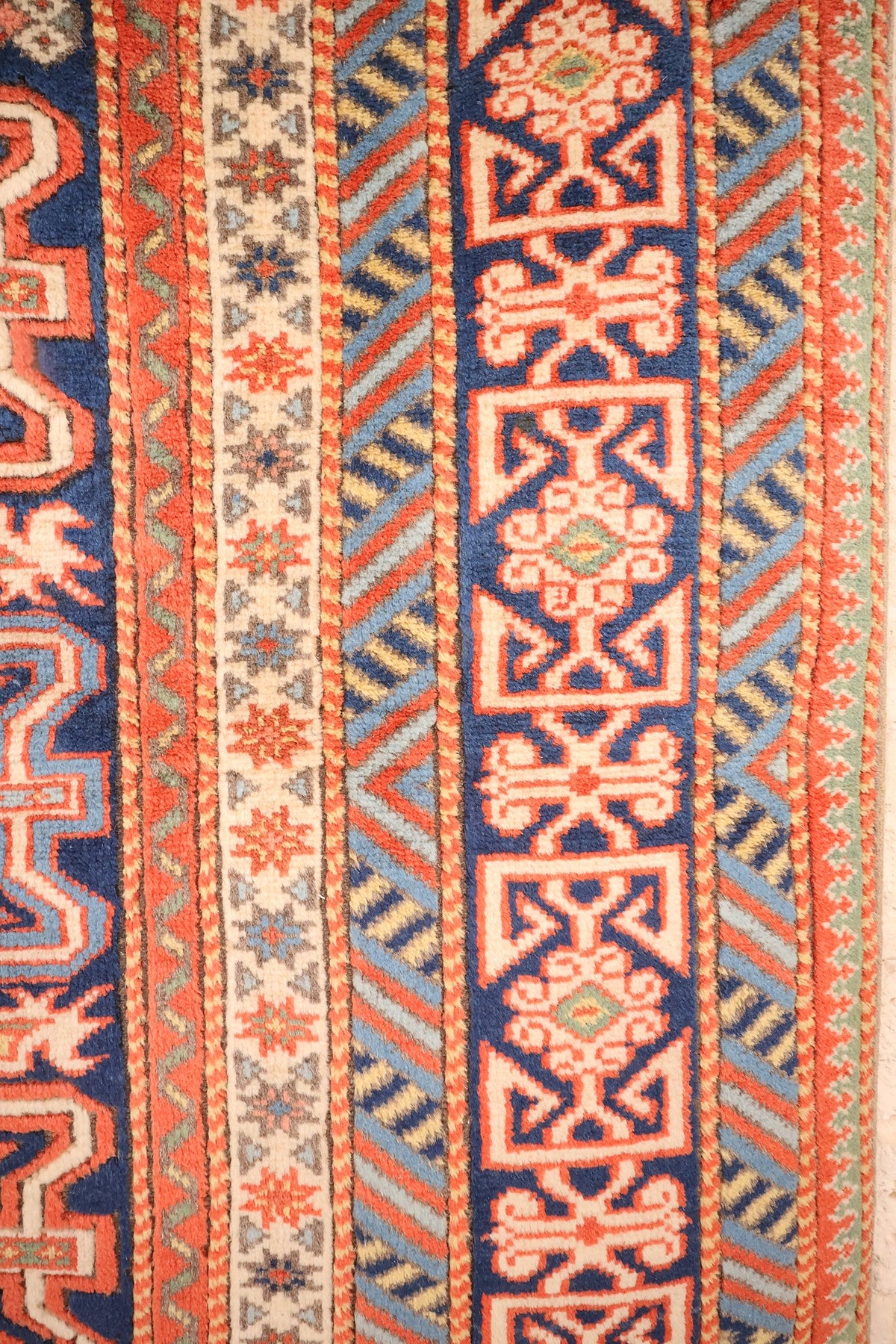 Bordures du tapis Hitit : cartouches ivoire, chevrons bleu clair et jaune, étoiles