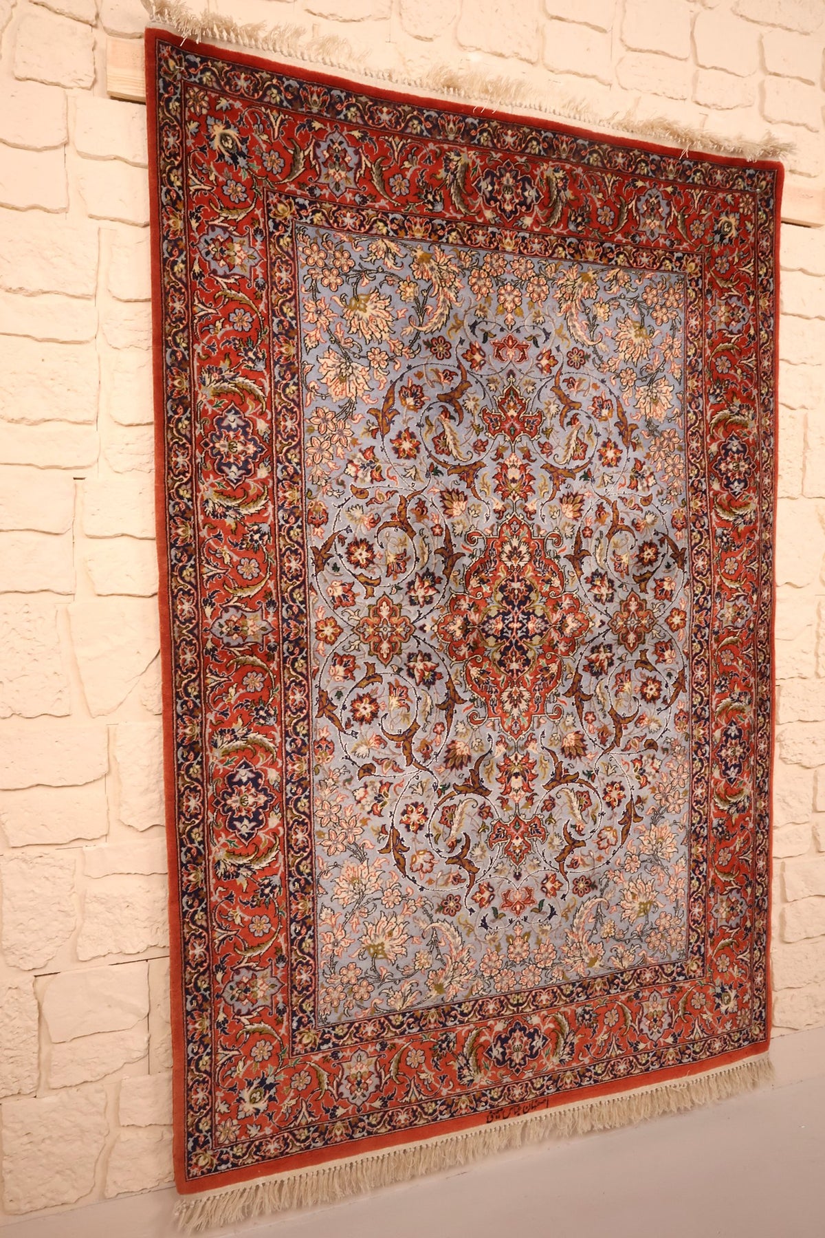 Tapis Ispahan noué à la main vu de biais, large bordure rouge à rinceaux fleuris