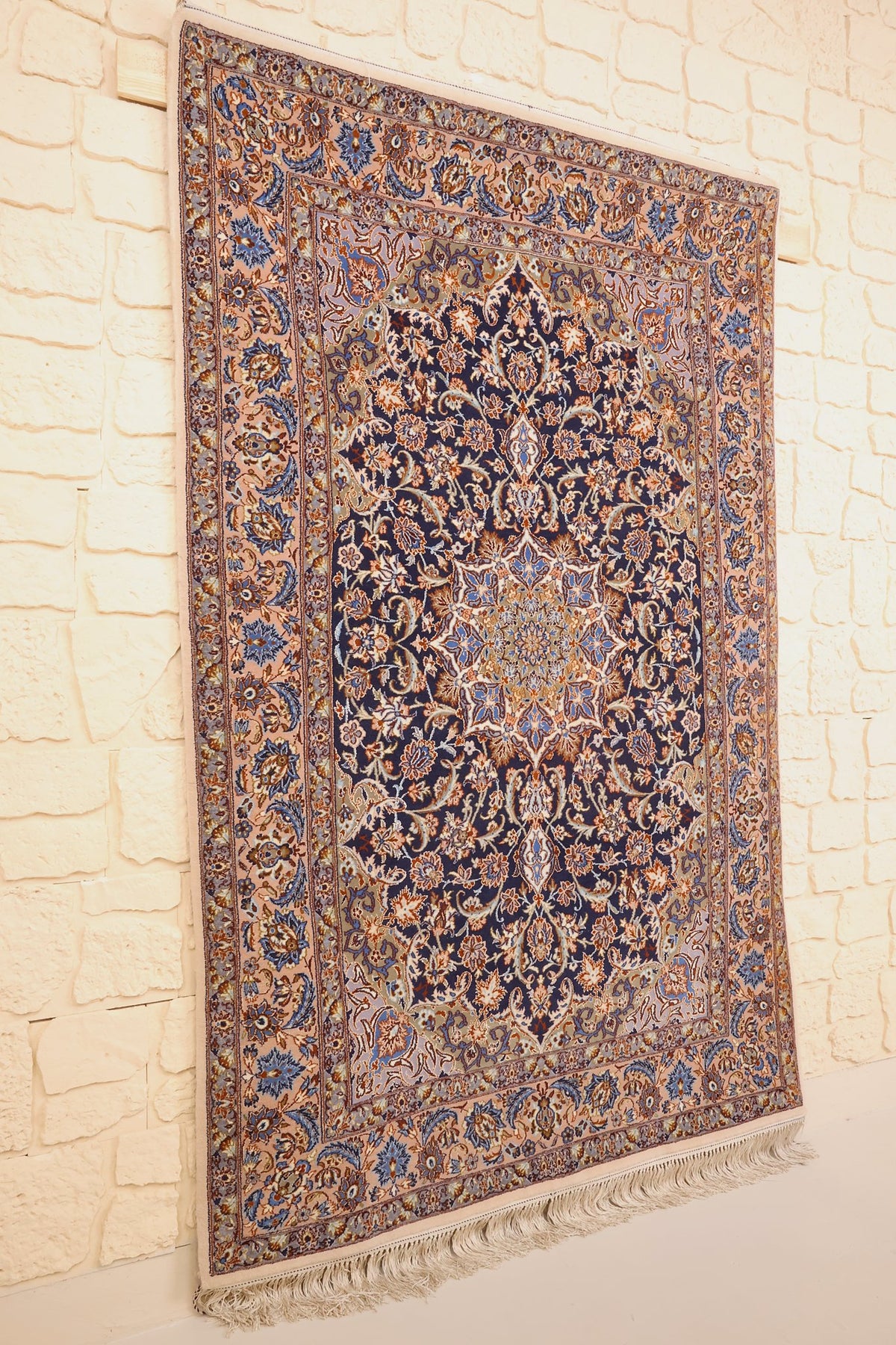 Tapis Ispahan en laine noué à la main, vue de biais contre un mur clair