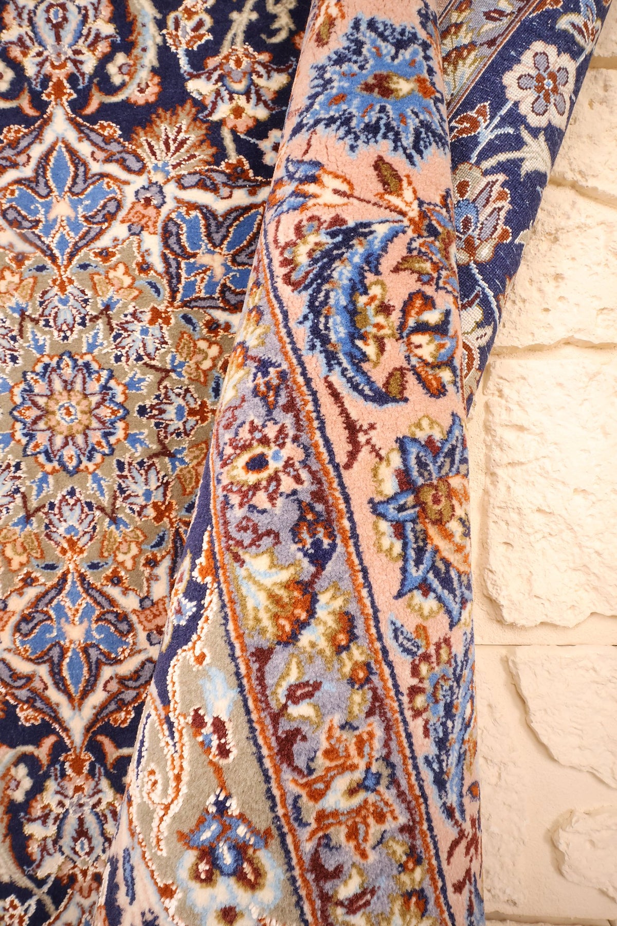 Tapis Ispahan en laine roulé sur un angle, bordure saumon et champ bleu