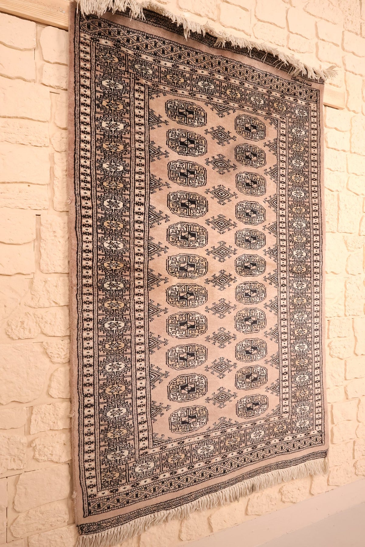 Tapis Karachi beige et noir en laine, vue de biais sur le champ à gols répétés