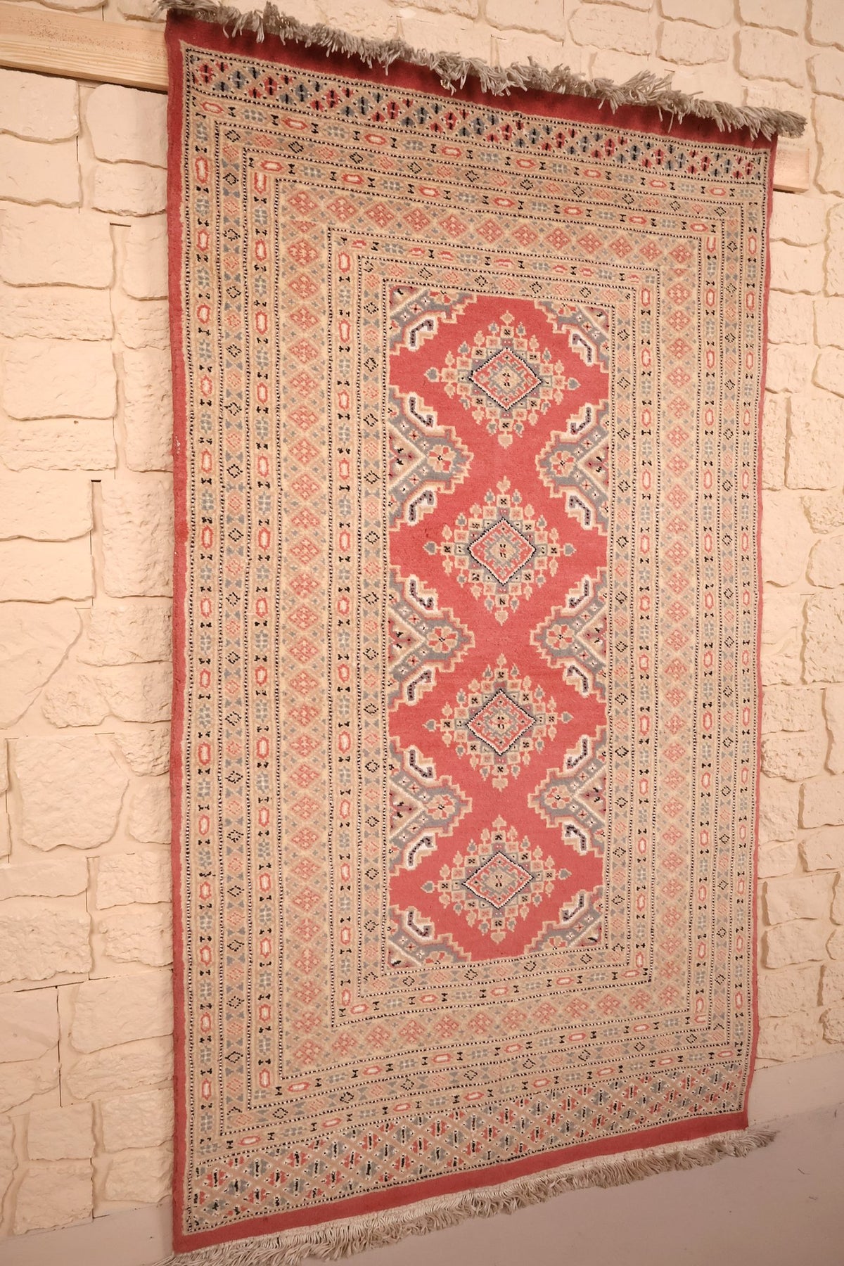 Vue de biais du tapis Karachi rose en laine, franges claires aux deux extrémités