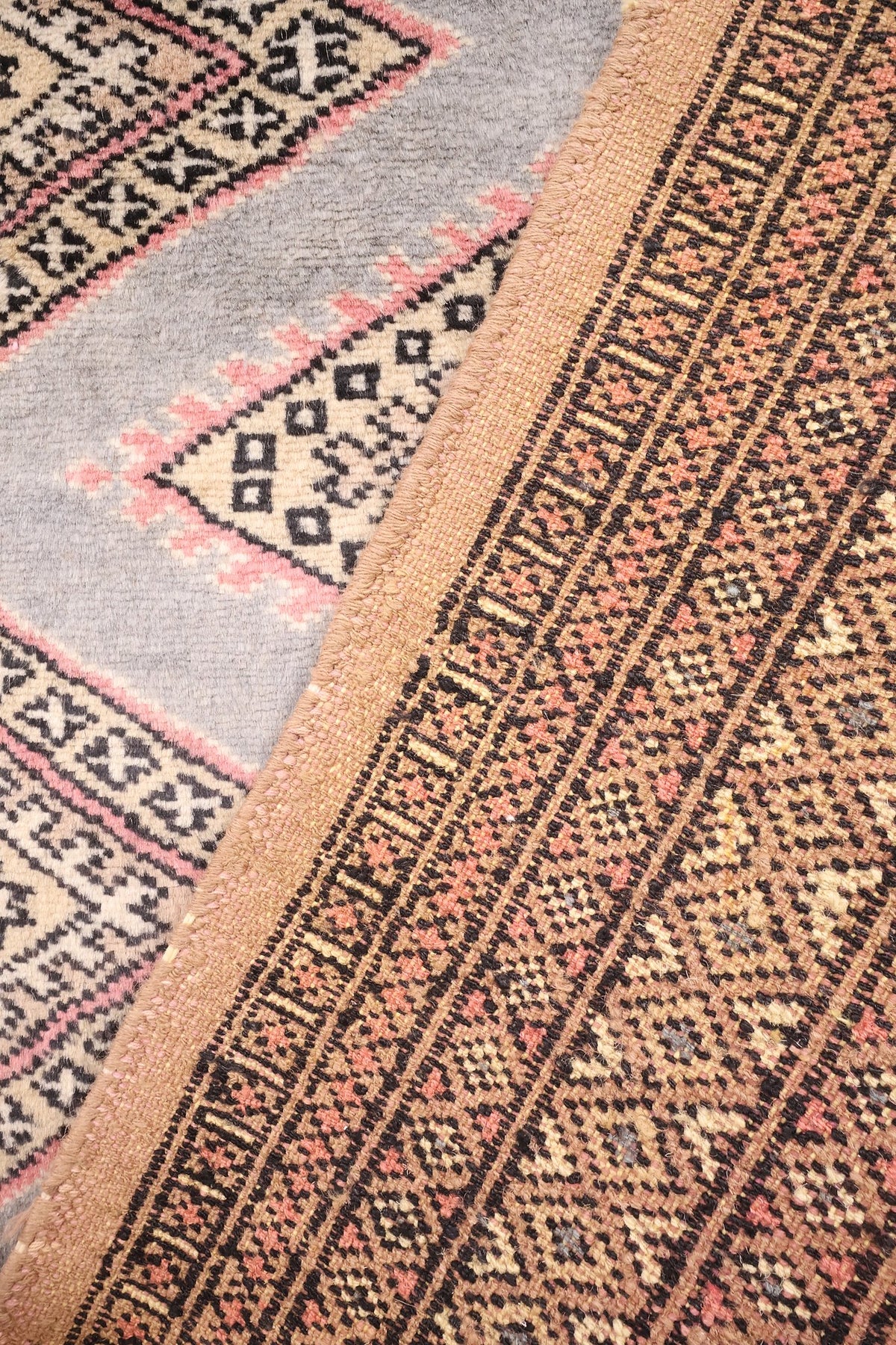Coin replié du tapis Boukhara, envers aux motifs géométriques beige et rose