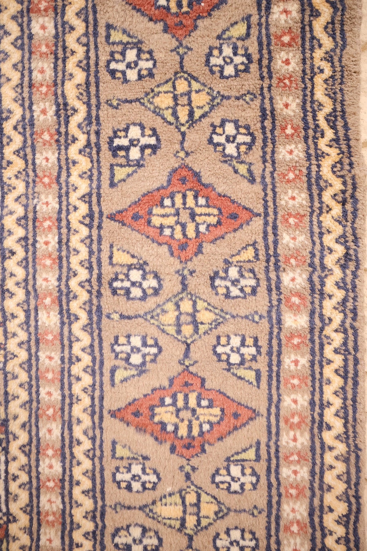 Bordure du tapis Karachi : losanges orange et fleurons blancs entre galons ondulés