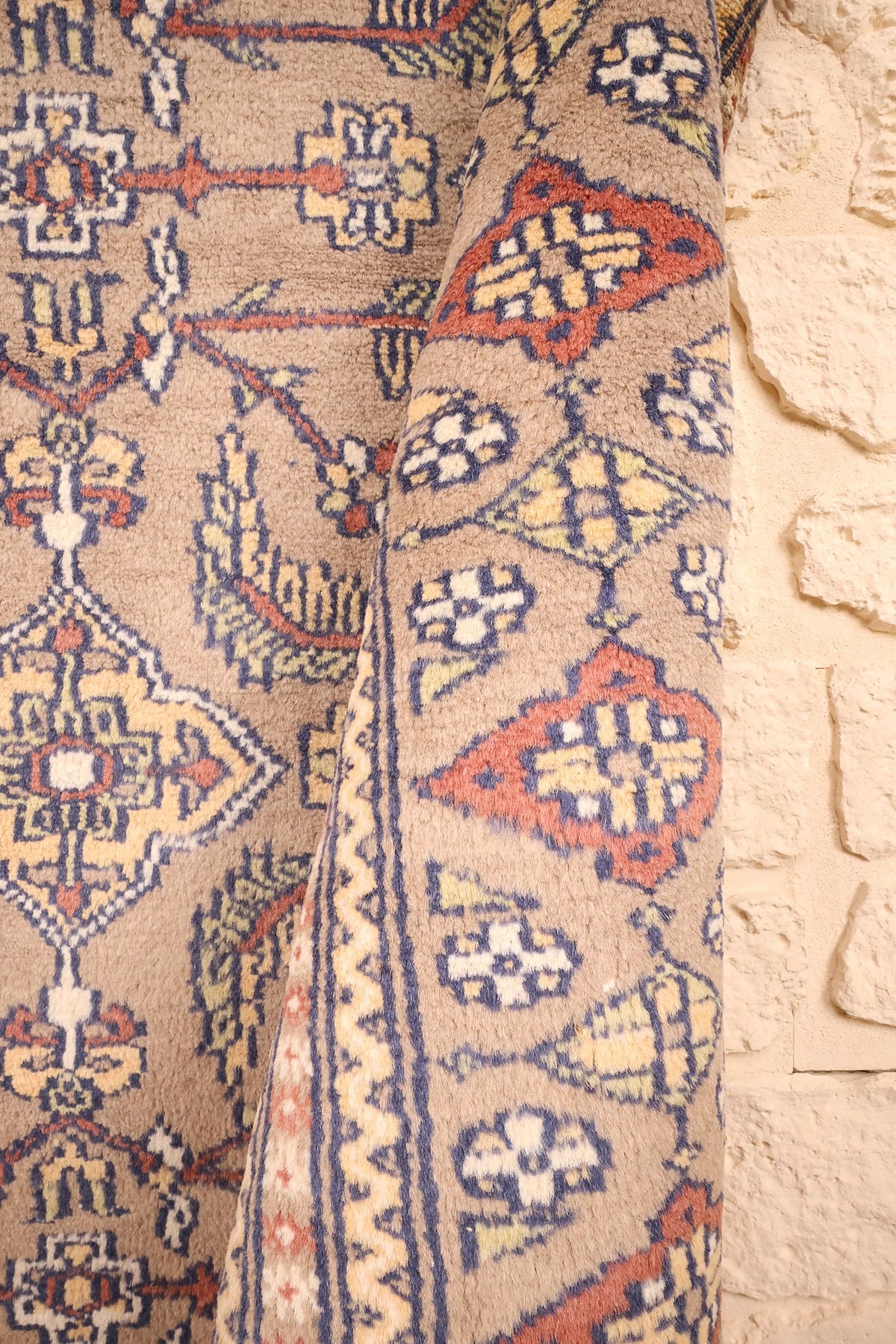 Coin replié du tapis Karachi beige, motifs bleu marine et orange brique de près