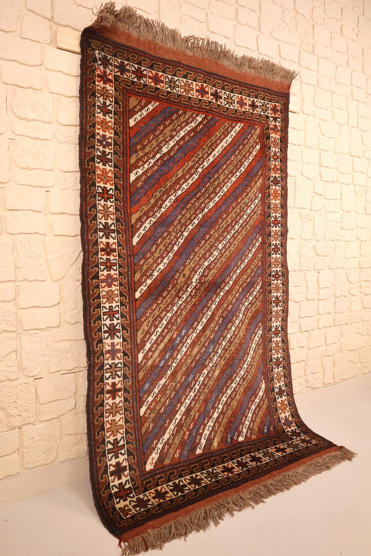 Vue de biais du tapis marron et rouge, bordure ivoire à étoiles et franges aux deux bouts