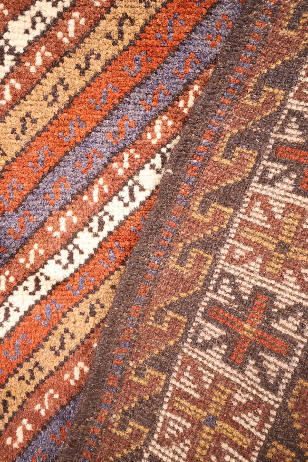 Coin replié du tapis marron, rayures du champ et bande brun foncé à crochets