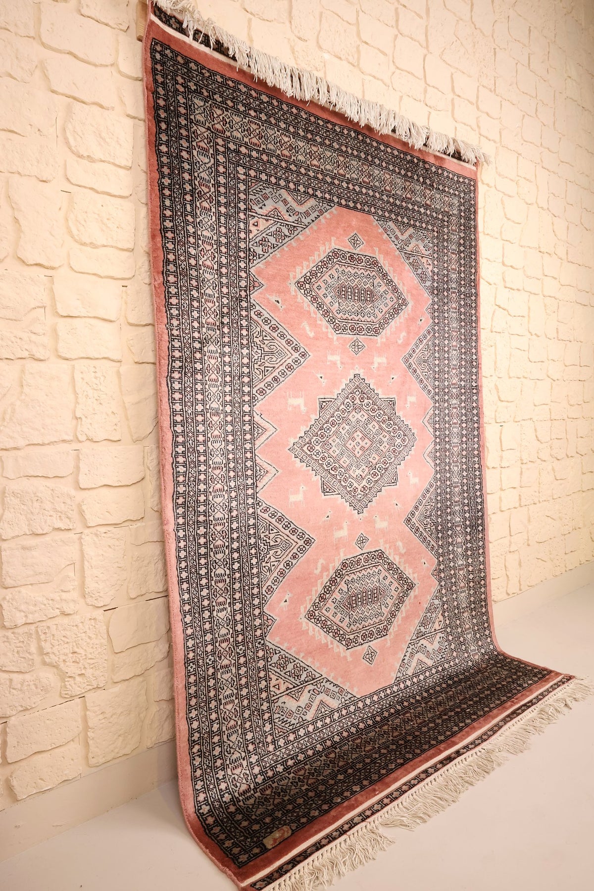 Tapis Boukhara en laine noué à la main, vue de biais contre un mur clair