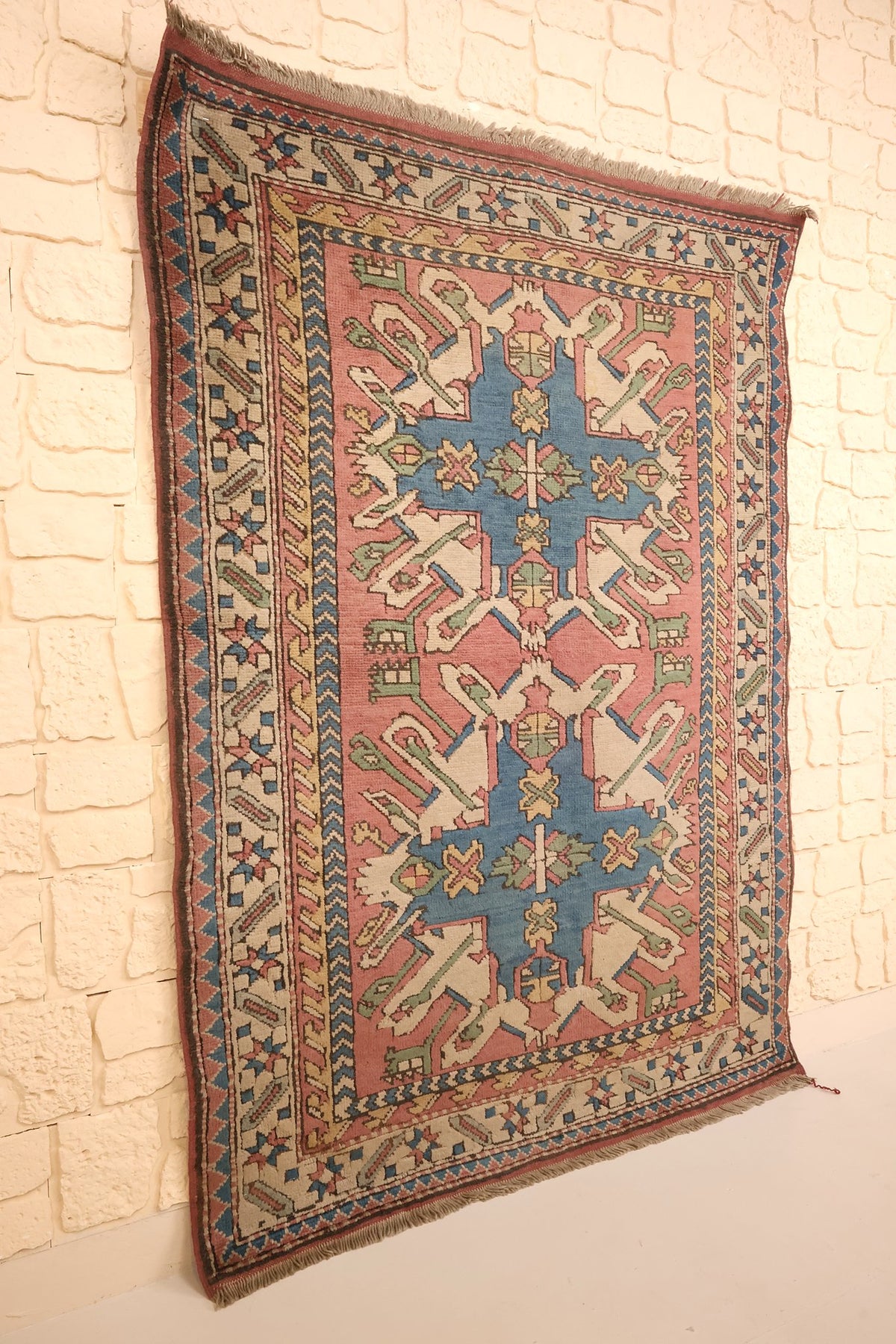 Tapis Kars rose et bleu en laine, vue de biais sur le mur clair