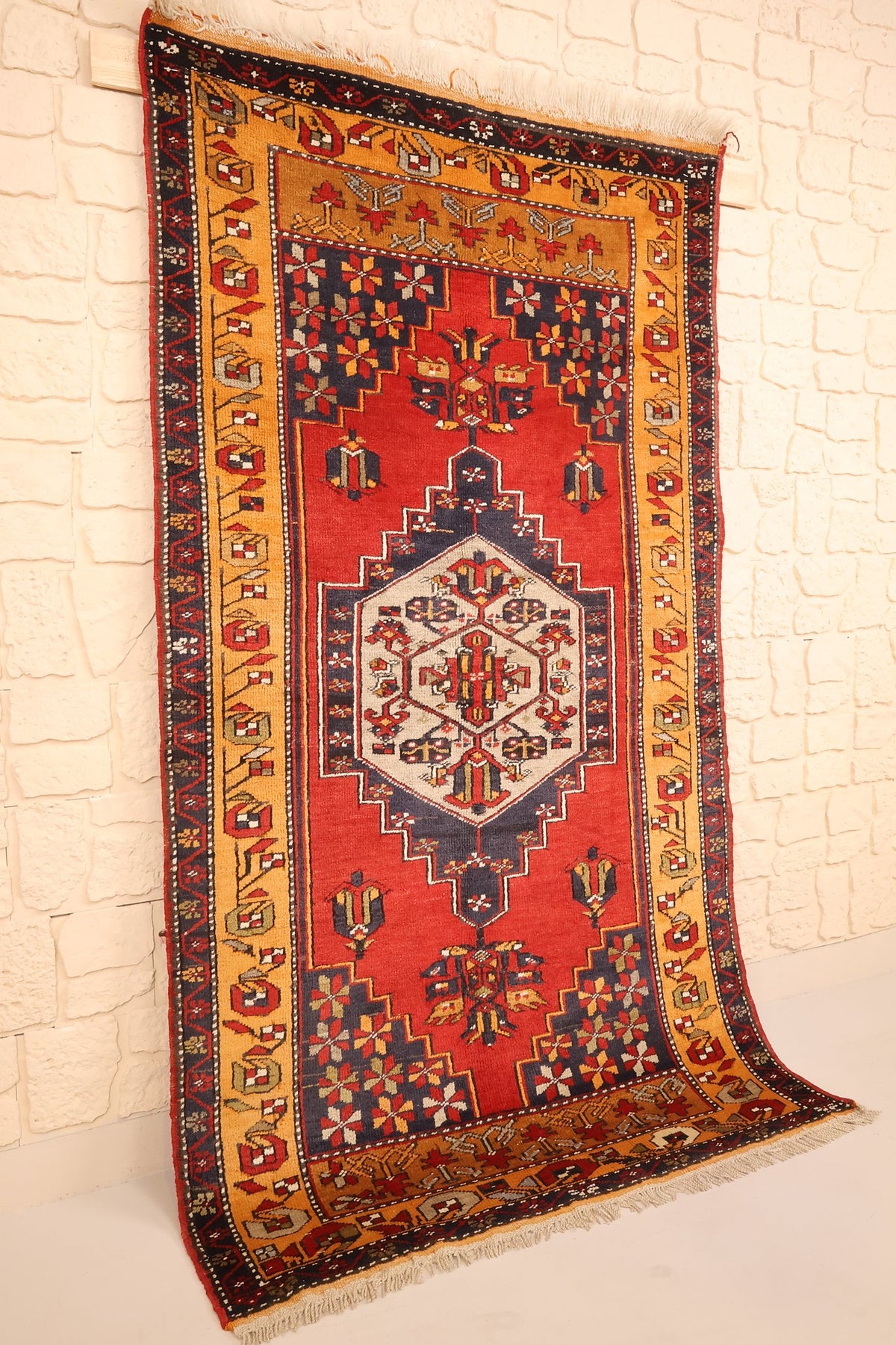 Tapis Kars rectangulaire rouge et orange, vue de biais contre un mur clair