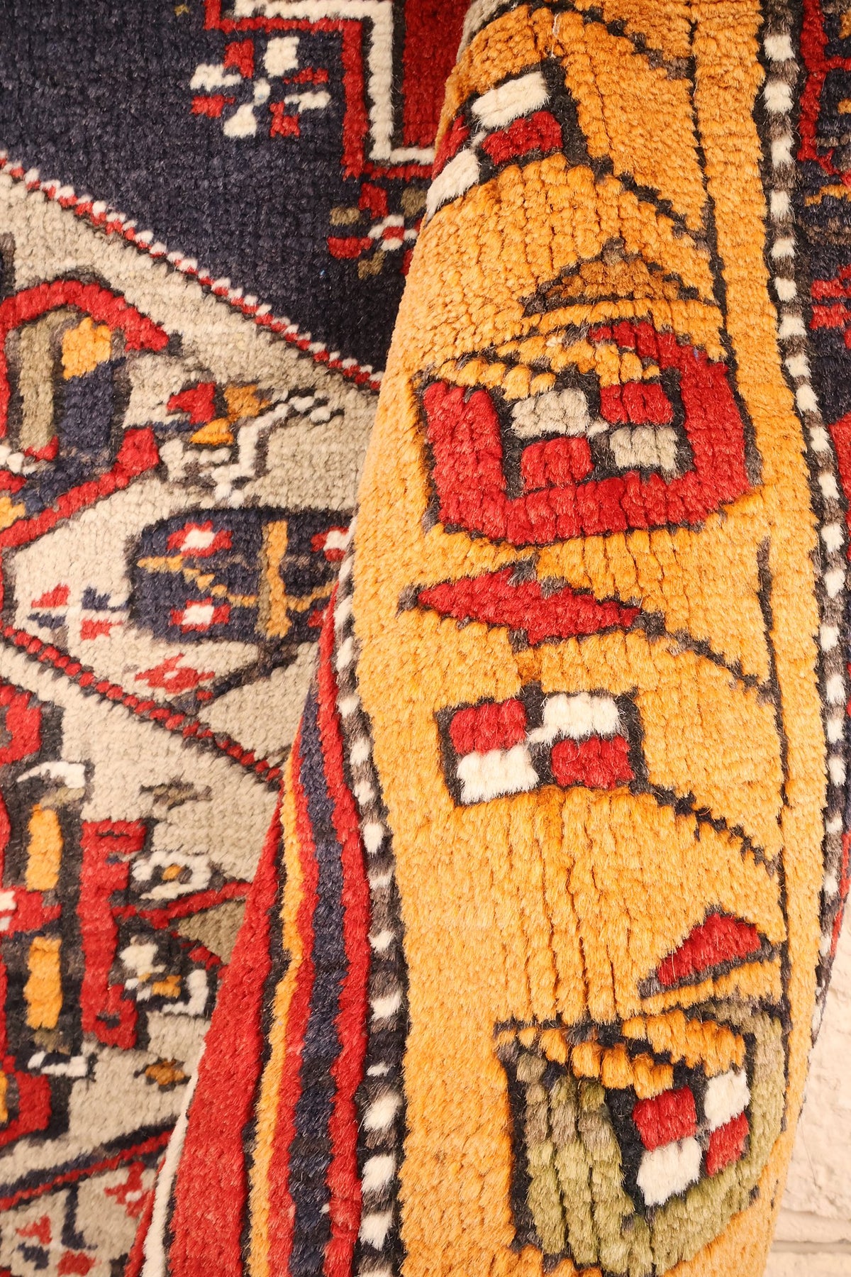 Coin replié du tapis Kars, bordure orangée et motifs en damier rouge et blanc
