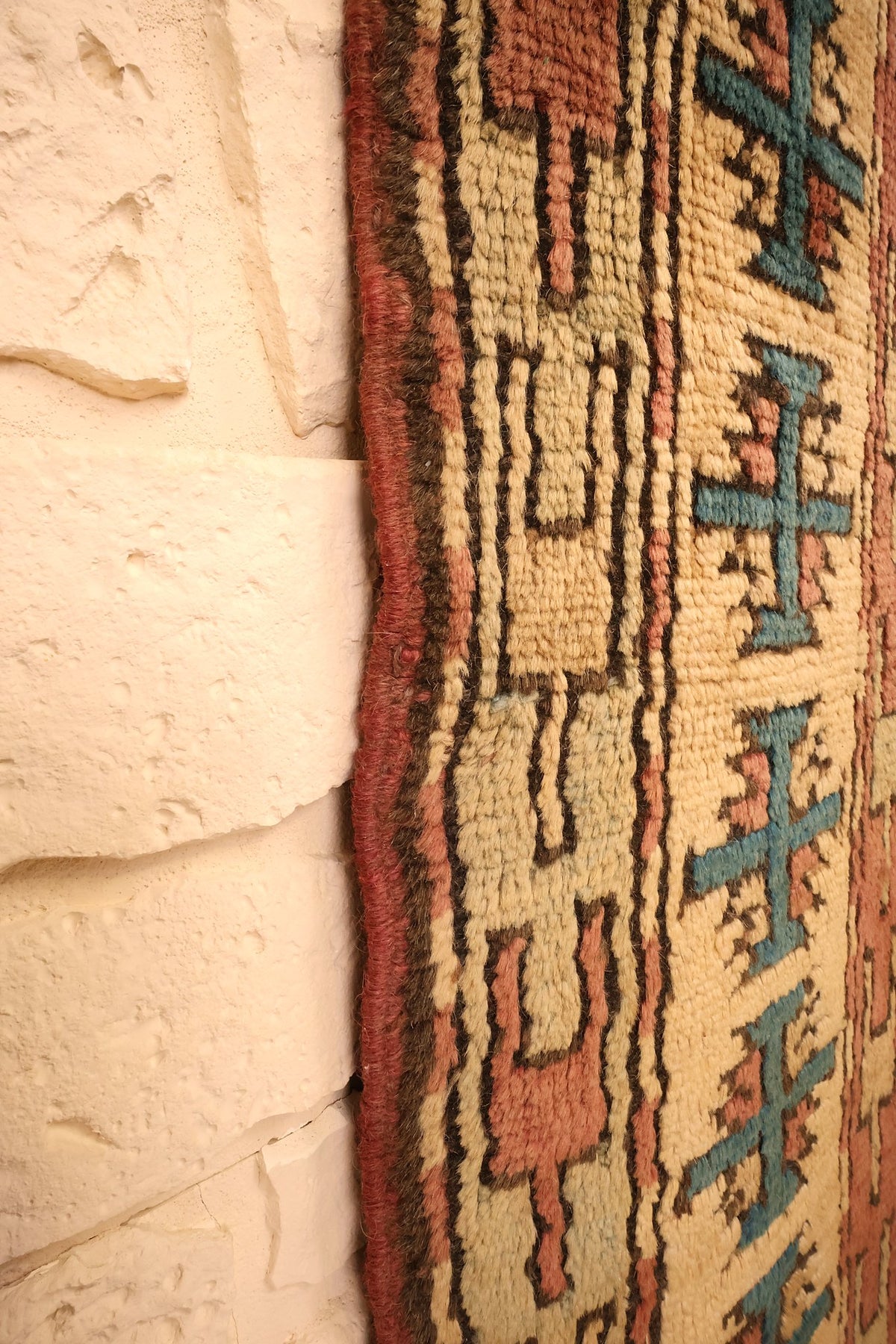 Lisière du tapis Kars beige contre un mur clair, bande à croix bleues