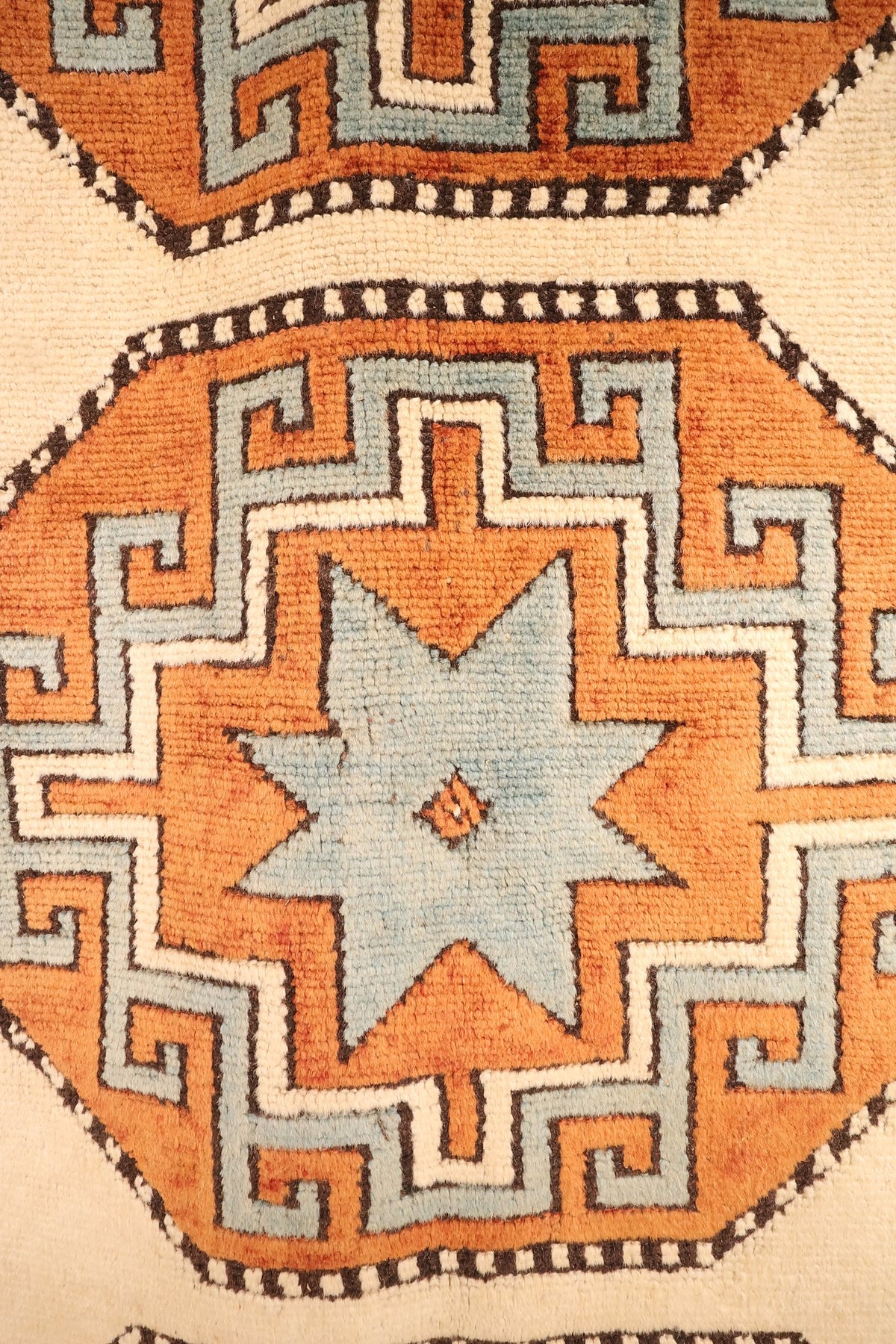 Détail d'un médaillon orange à étoile bleu clair et crochets en grecque, tapis Kars