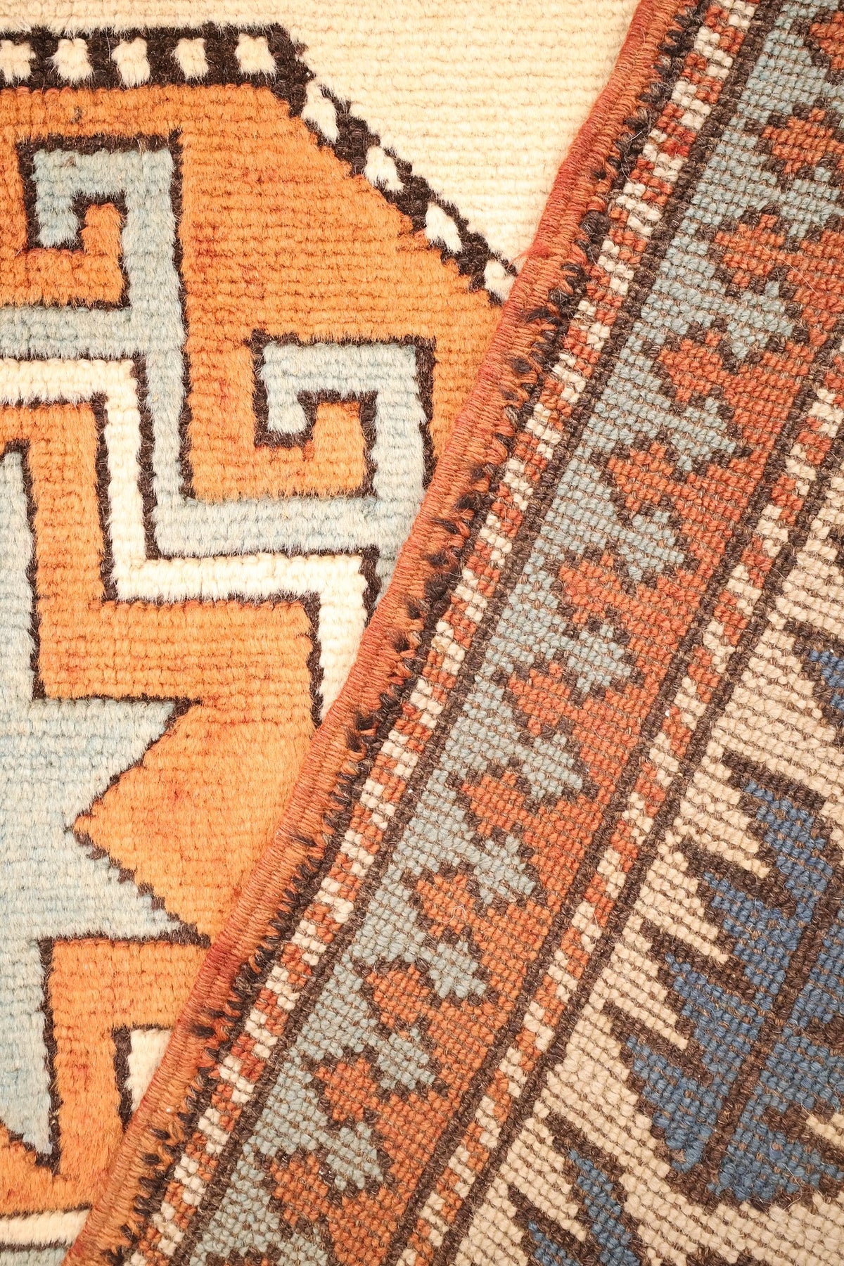 Coin replié du tapis Kars, lisière brune et ligne dentelée brun et blanc