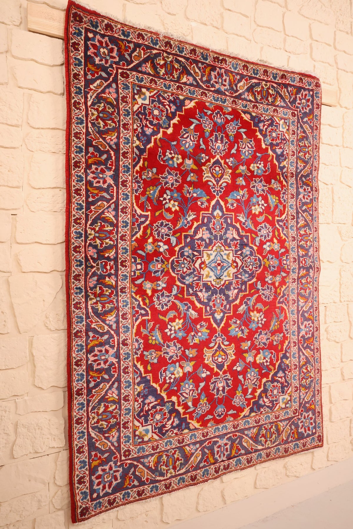 Tapis Kashan rectangulaire rouge et bleu vu de biais, champ fleuri et bordure à palmettes
