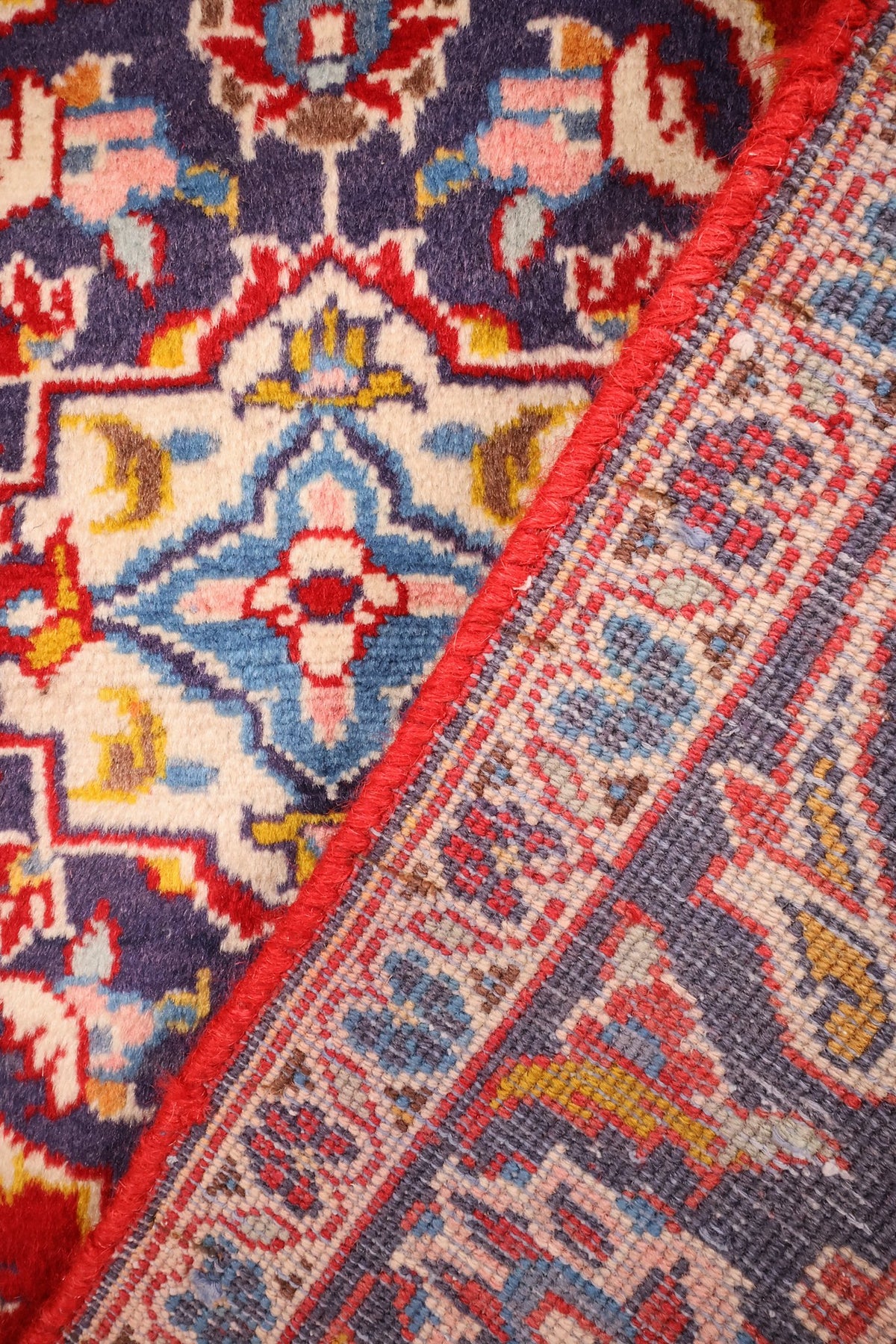 Envers du tapis Kashan, nœuds visibles et reprise des tons rouge, bleu et ivoire