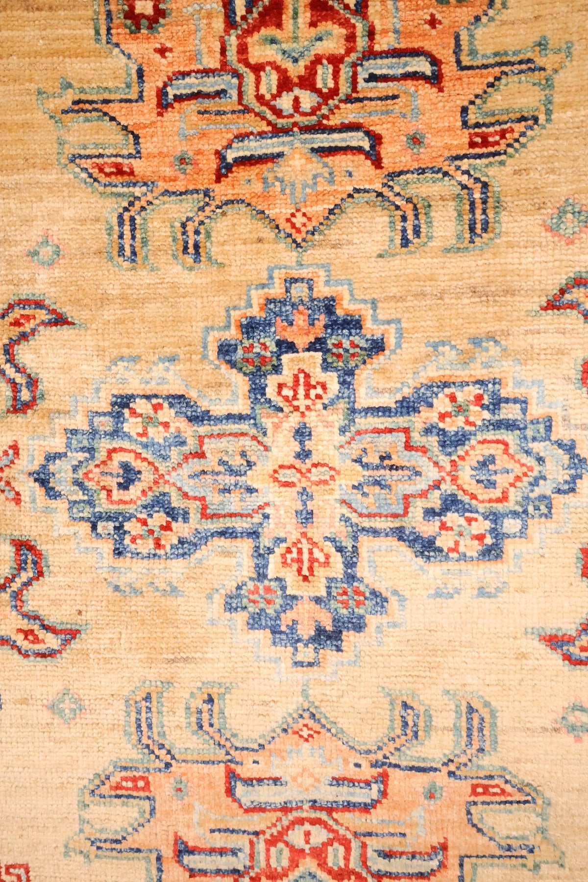 Détail d'un médaillon anguleux bleu et rouge au centre du tapis Kazak beige