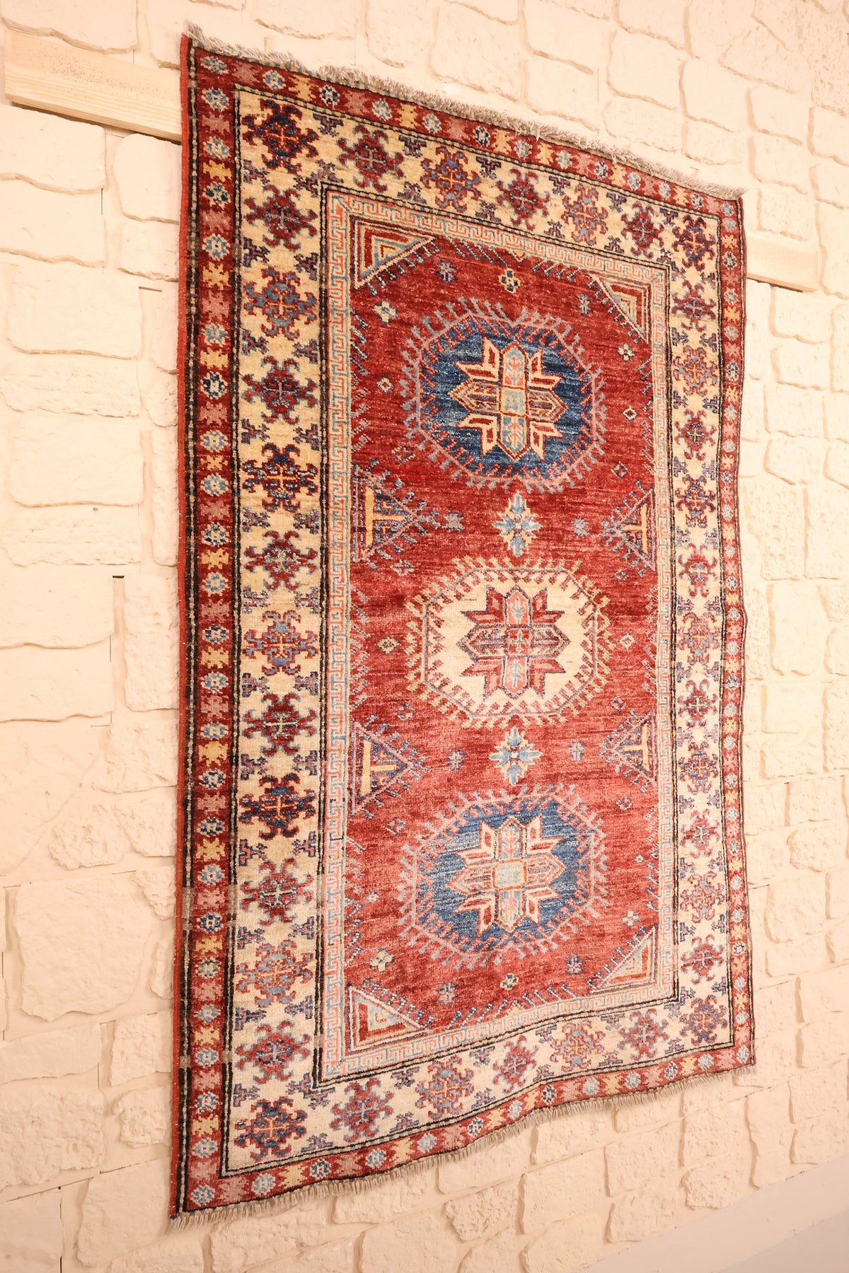 Tapis Kazak rectangulaire en laine, vue de biais sur le champ rouge brique
