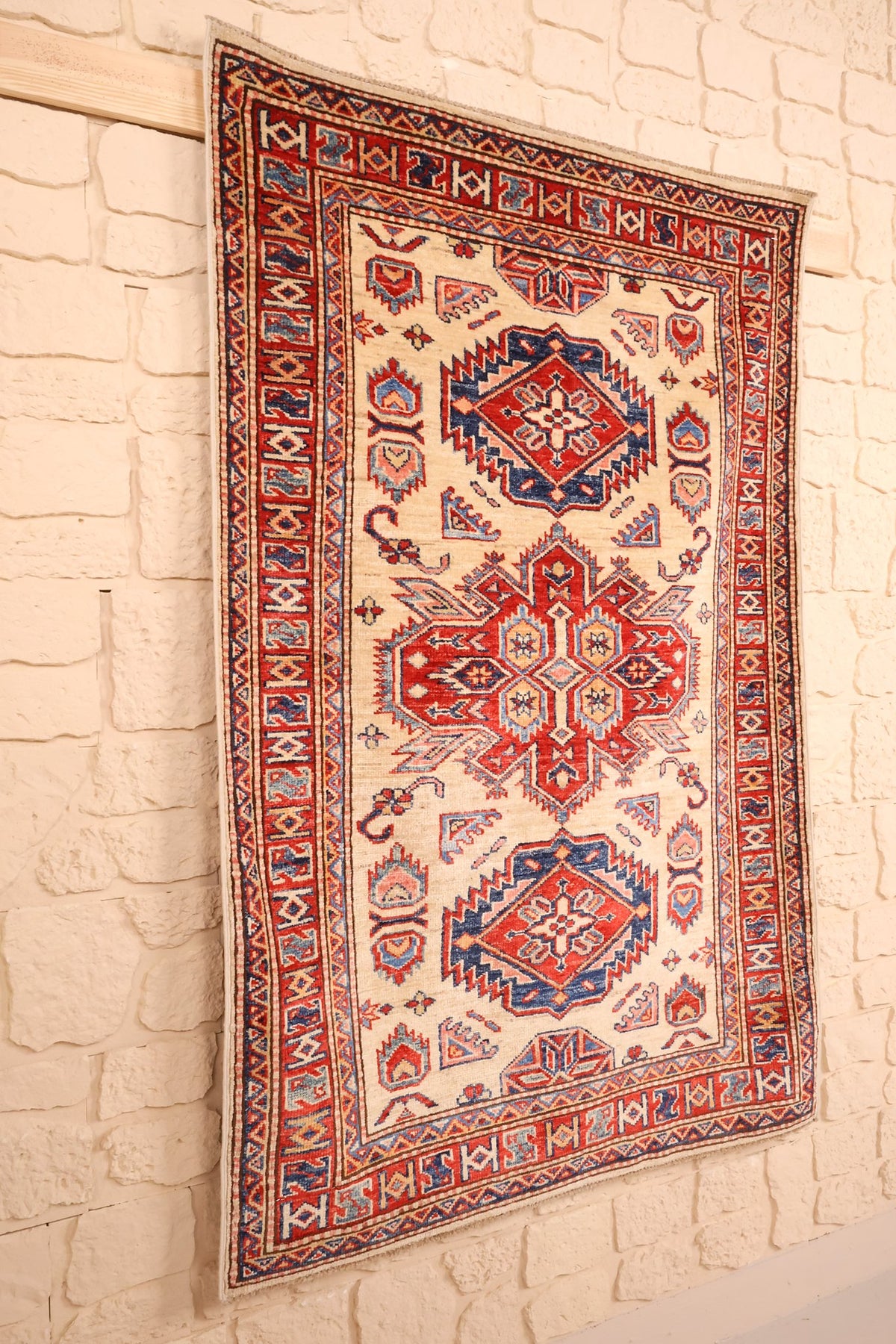 Tapis Kazak en laine à dominante beige, vue de biais sur un mur clair