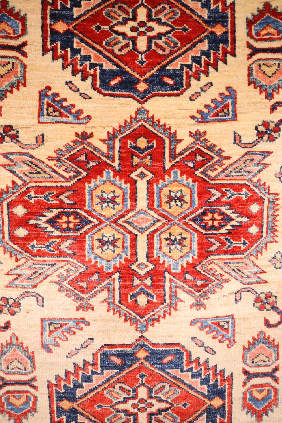 Détail du médaillon central rouge à crochets et étoiles du tapis Kazak beige