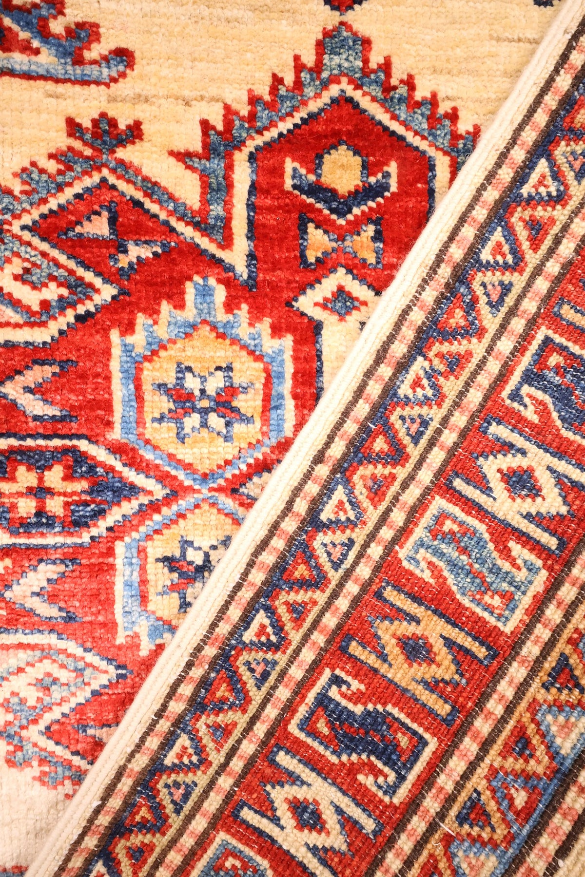 Coin replié du tapis Kazak, champ beige et bordure géométrique côte à côte