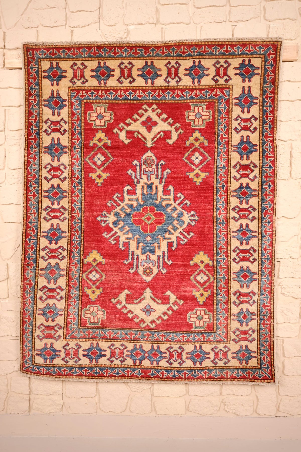 Tapis Kazak rouge 142 × 108 cm, vue d'ensemble avec médaillon étoilé bleu et ivoire