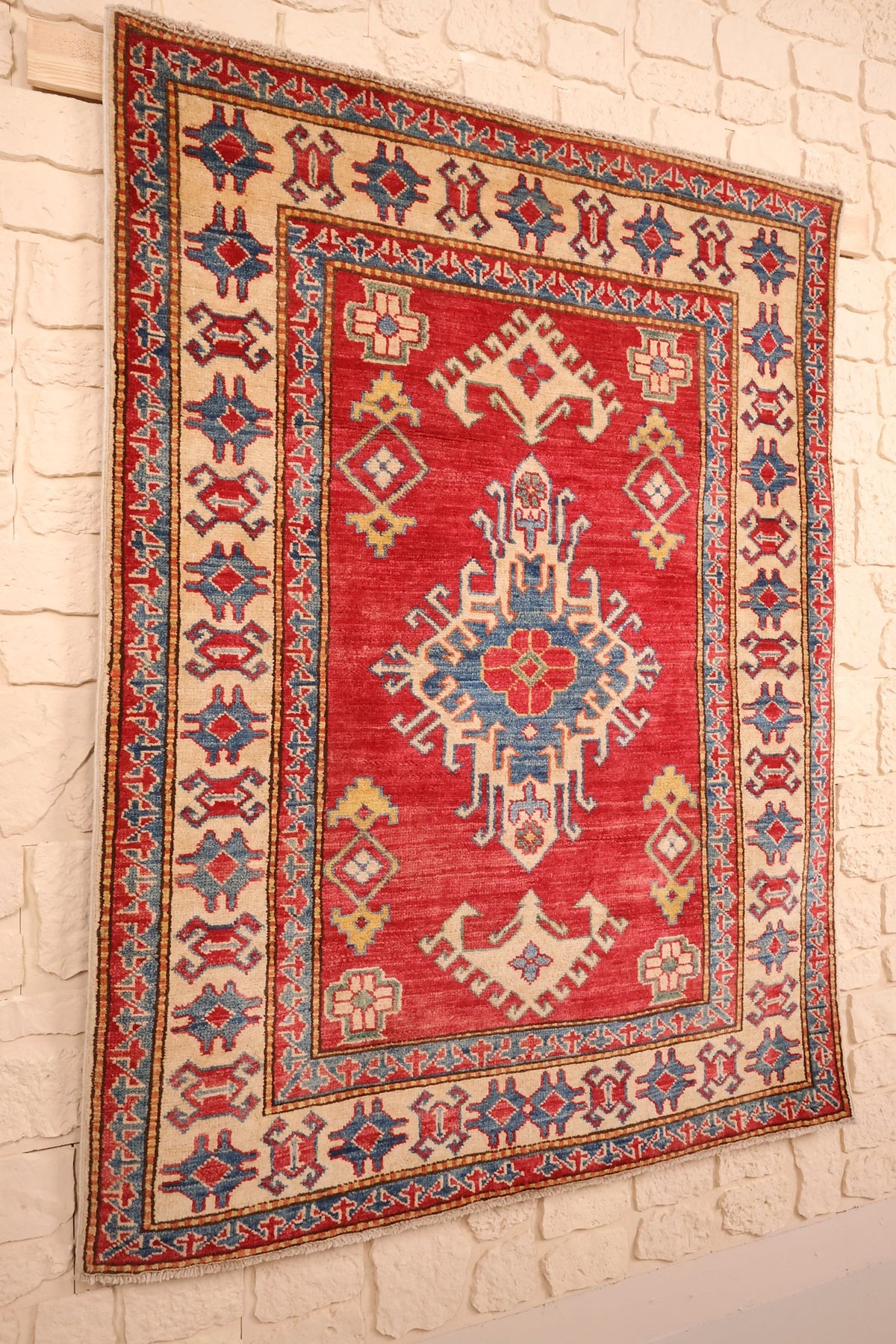 Tapis Kazak rectangulaire en laine, vue de biais du champ rouge et des bordures ivoire