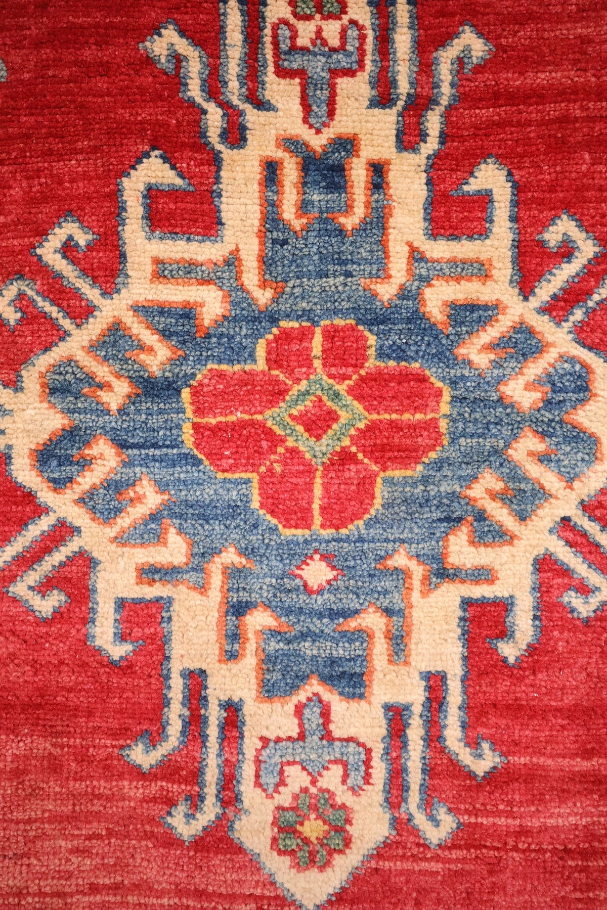 Détail du médaillon central crocheté bleu et ivoire du tapis Kazak rouge