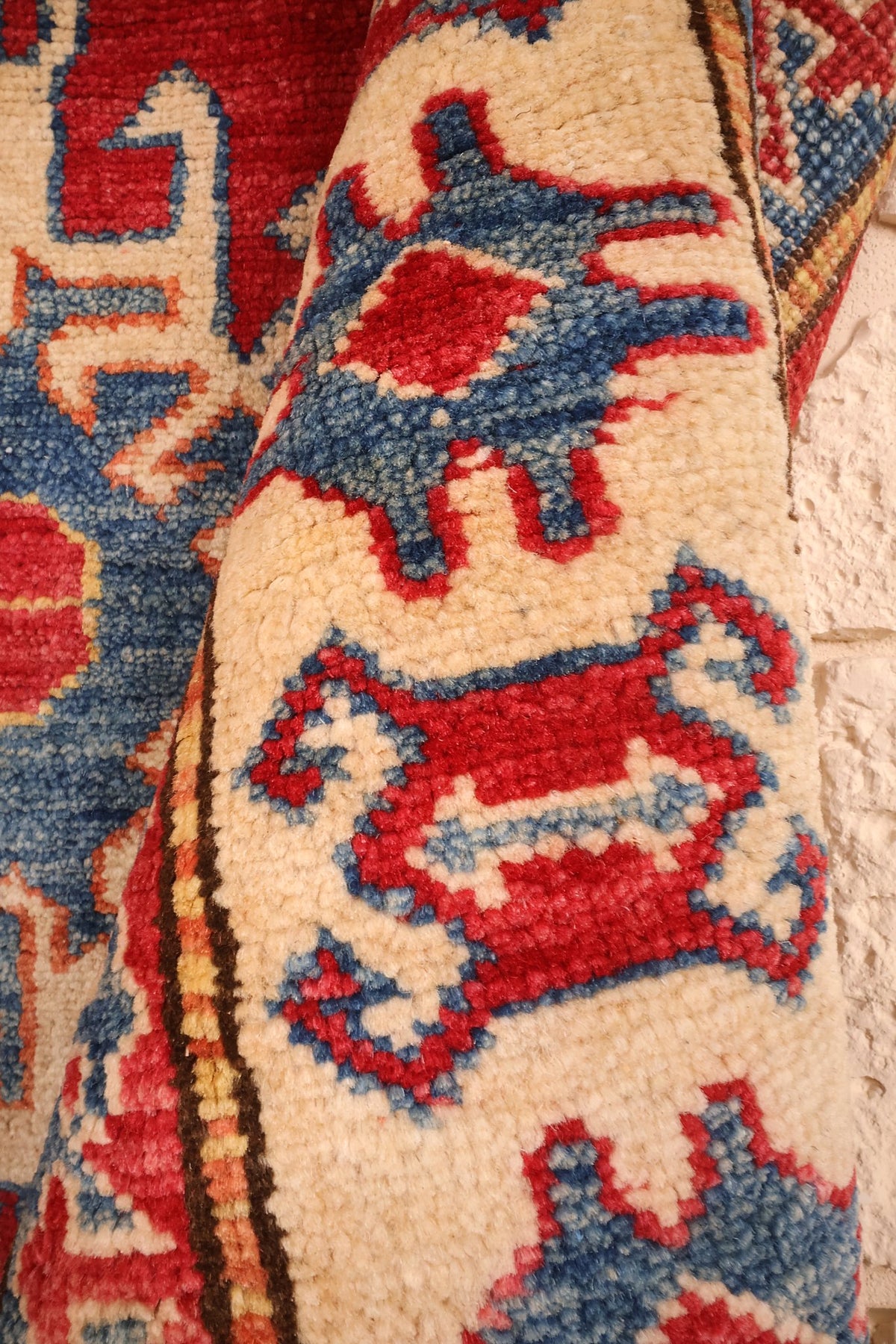 Coin replié du tapis Kazak, motifs anguleux bleus et rouges sur fond ivoire