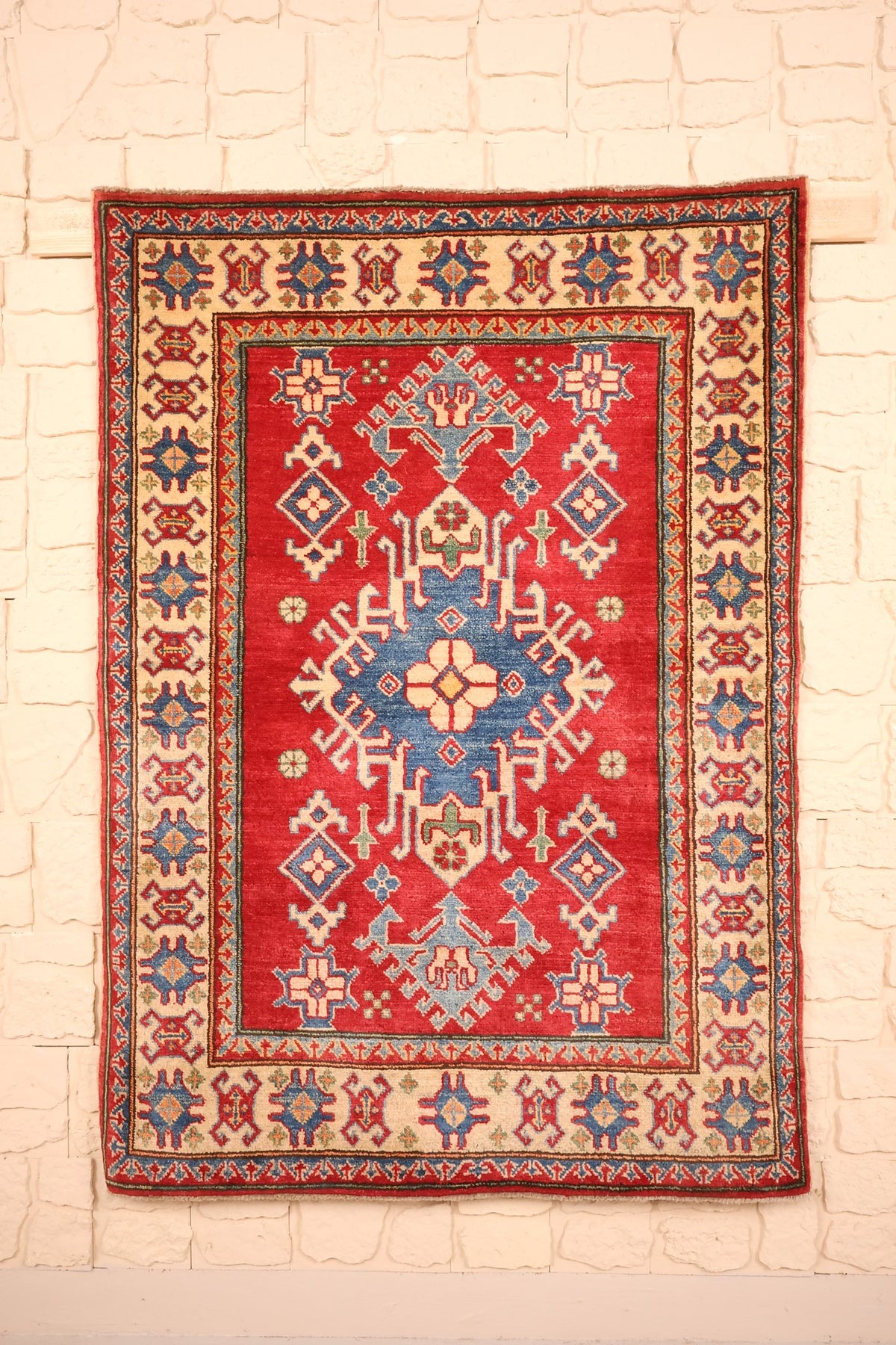 Tapis Kazak rouge 144 × 105 cm, vue d'ensemble avec médaillon central bleu à crochets