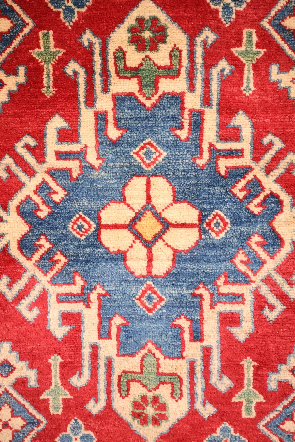 Détail du médaillon bleu à crochets et de la rosette ivoire du tapis Kazak rouge