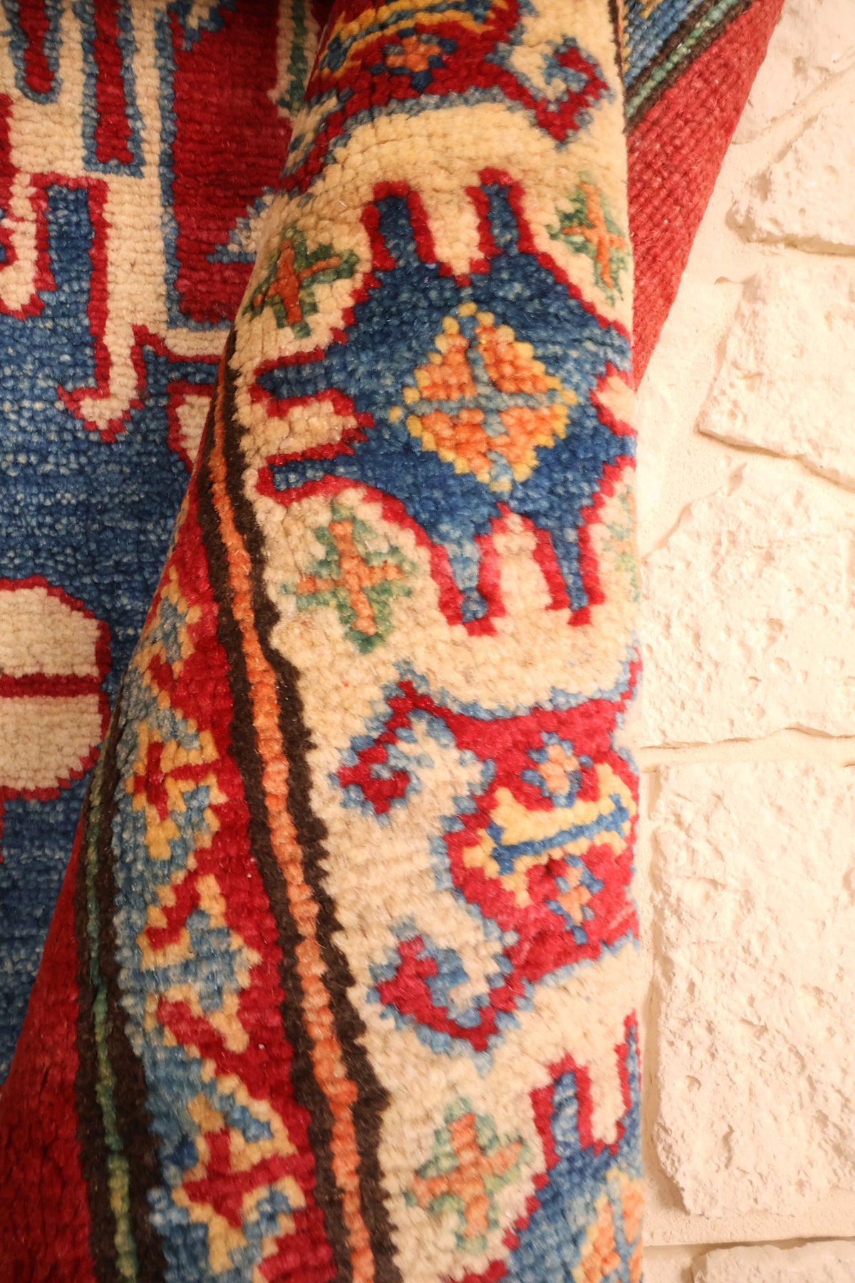 Coin replié du tapis Kazak rouge et bleu, épaisseur de la laine visible