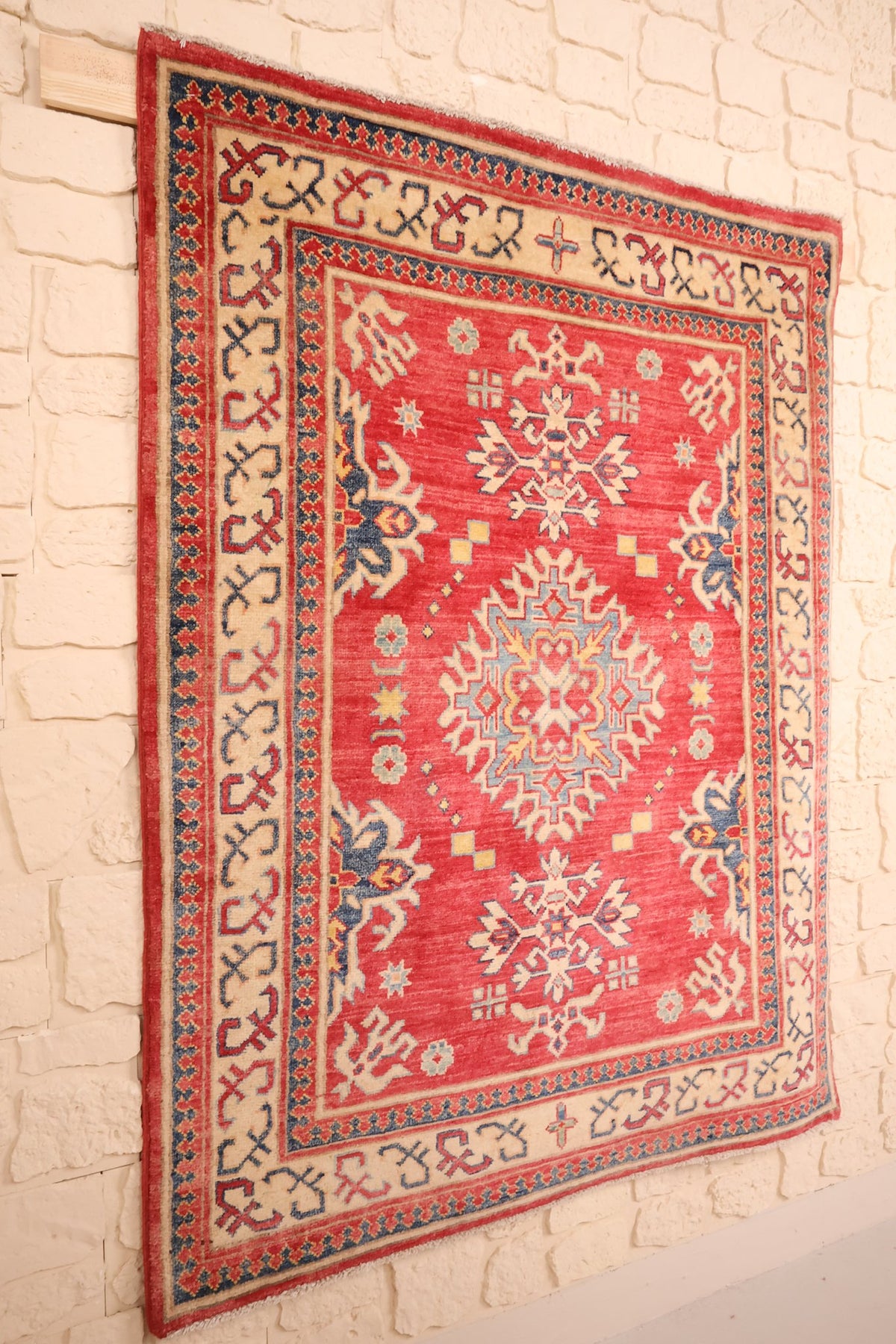 Tapis Kazak rouge et beige vu de biais, bordure ivoire à crochets anguleux