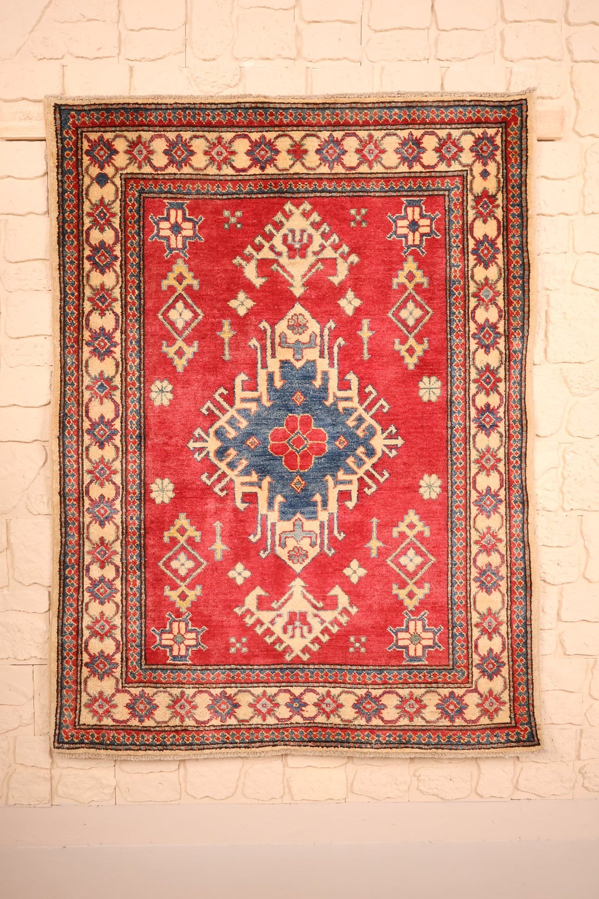 Tapis Kazak rouge 145 × 107 cm, vue d'ensemble du médaillon central bleu à crochets