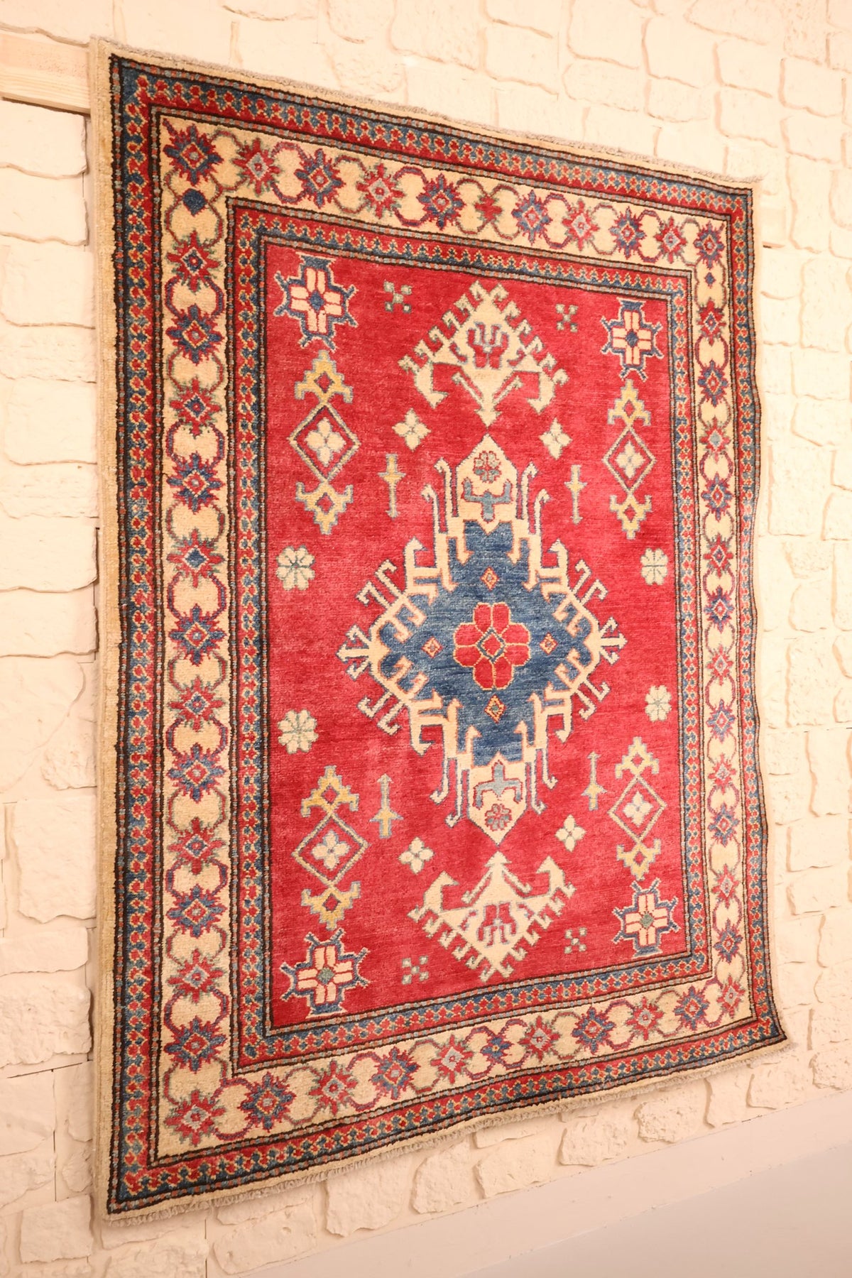 Tapis Kazak rouge et beige en laine, vue de biais sur le champ et ses bordures