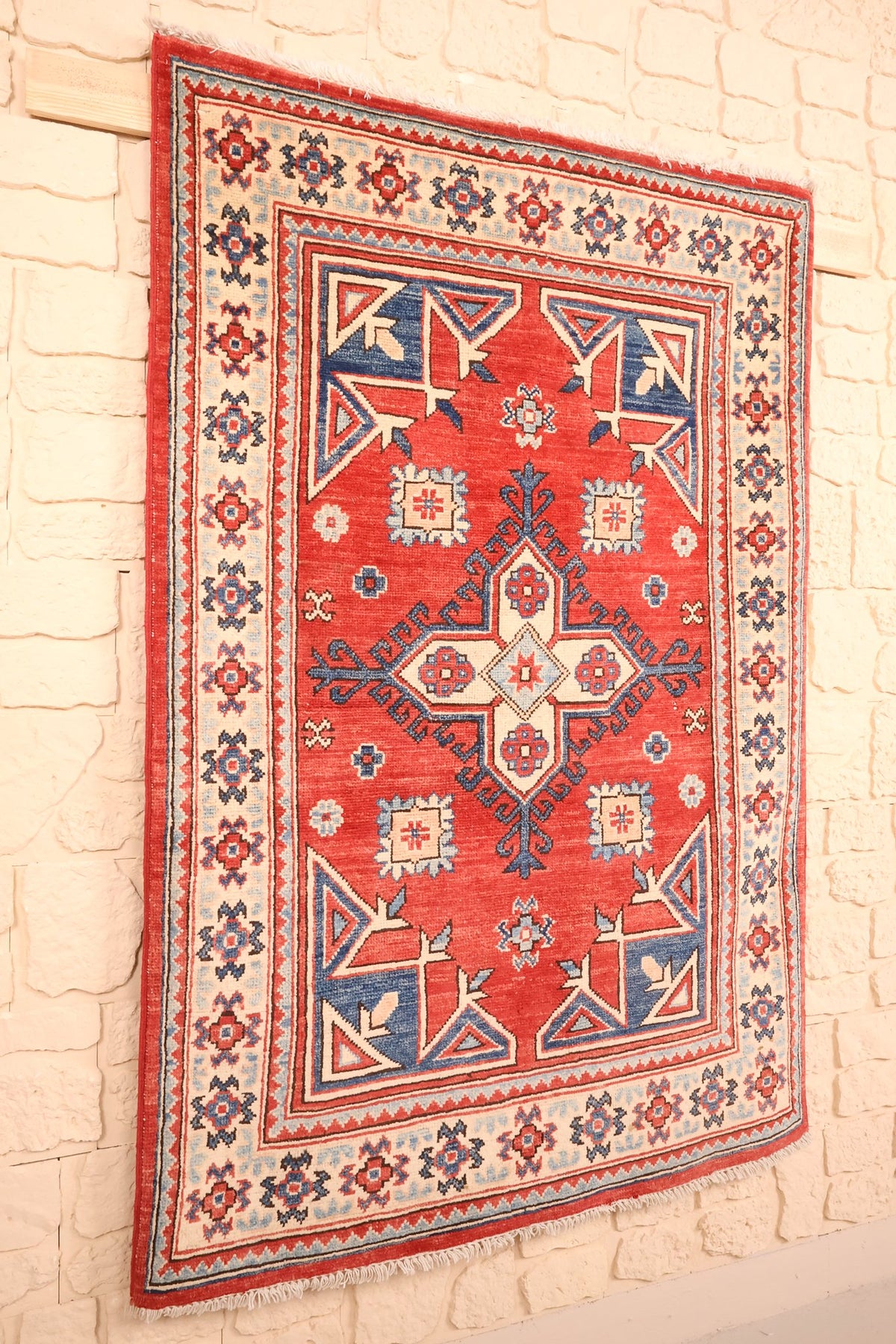 Tapis Kazak en laine rouge et bleu, vue de biais avec ses écoinçons bleu foncé