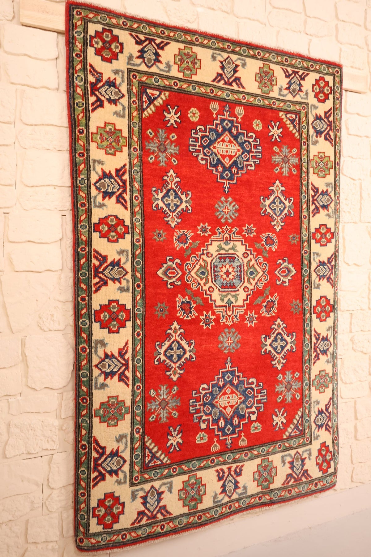 Tapis Kazak en laine rouge et beige, vue de biais sur le champ et sa bordure ivoire