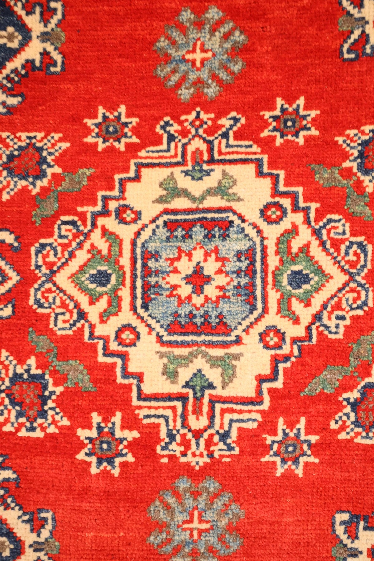 Détail du médaillon central ivoire à cœur bleu étoilé du tapis Kazak rouge