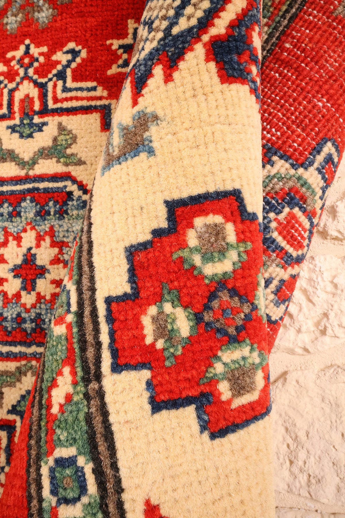 Coin replié du tapis Kazak, croix rouges de la bordure et champ rouge au second plan