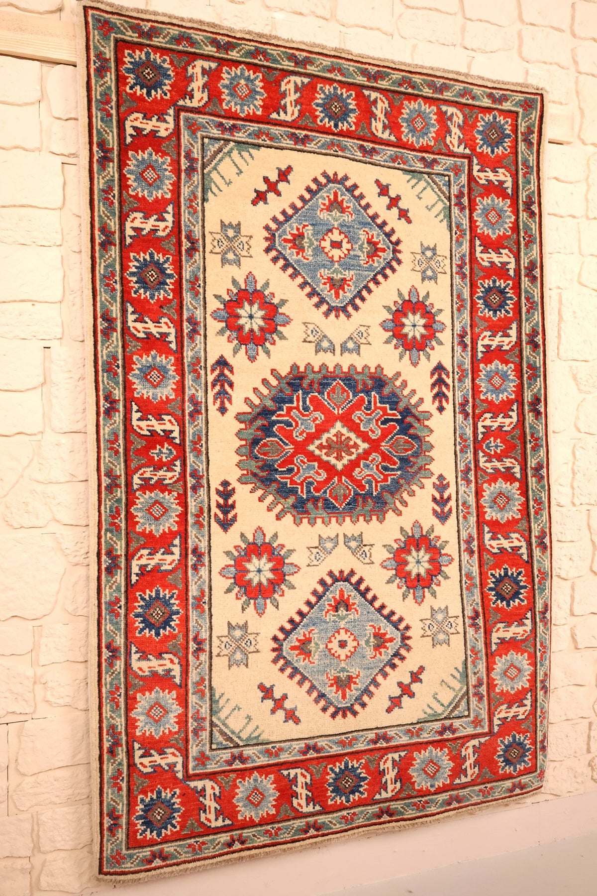 Tapis Kazak en laine noué à la main, vue de biais du champ ivoire et des bordures rouges