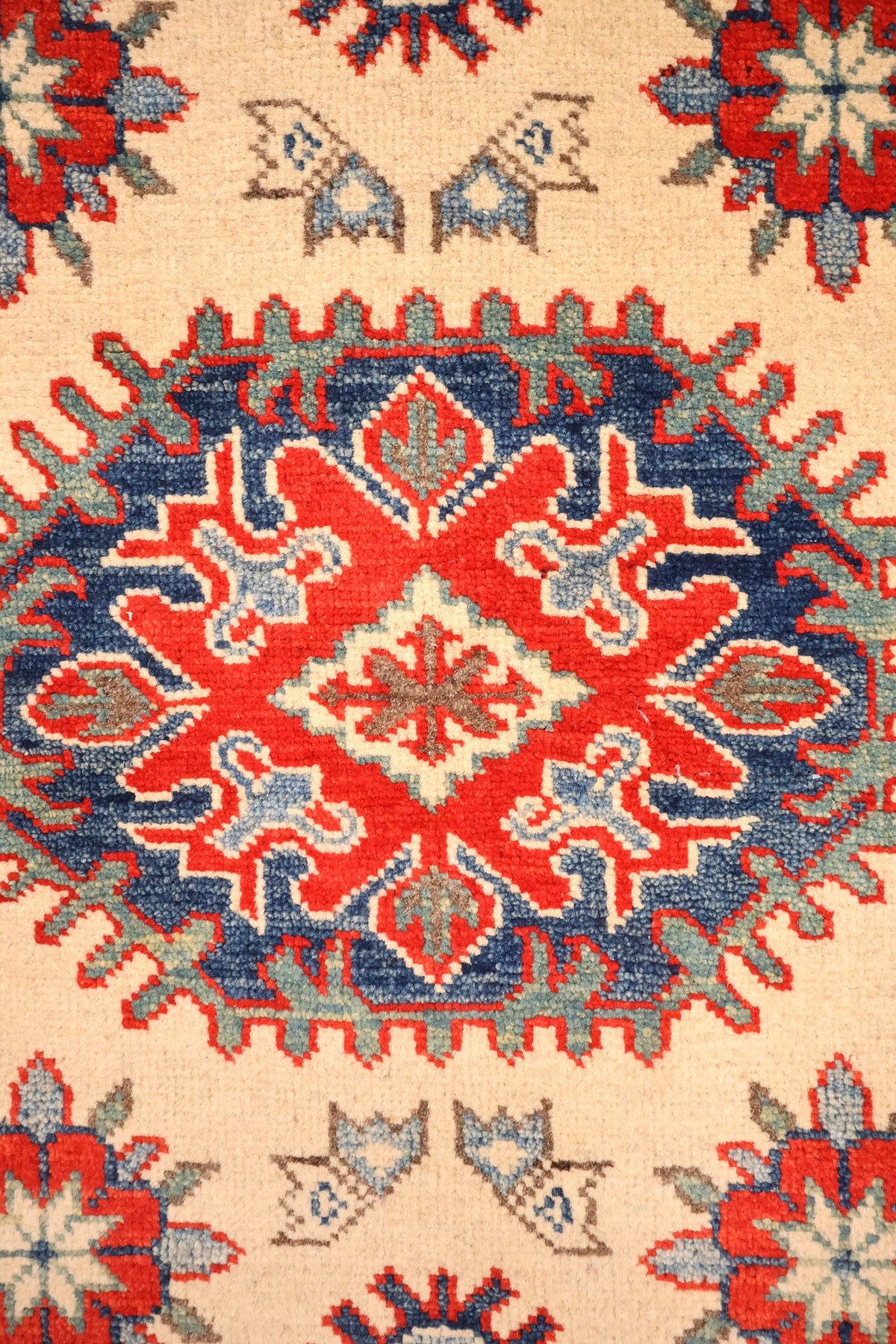 Détail du médaillon crénelé rouge et bleu au centre du tapis Kazak beige