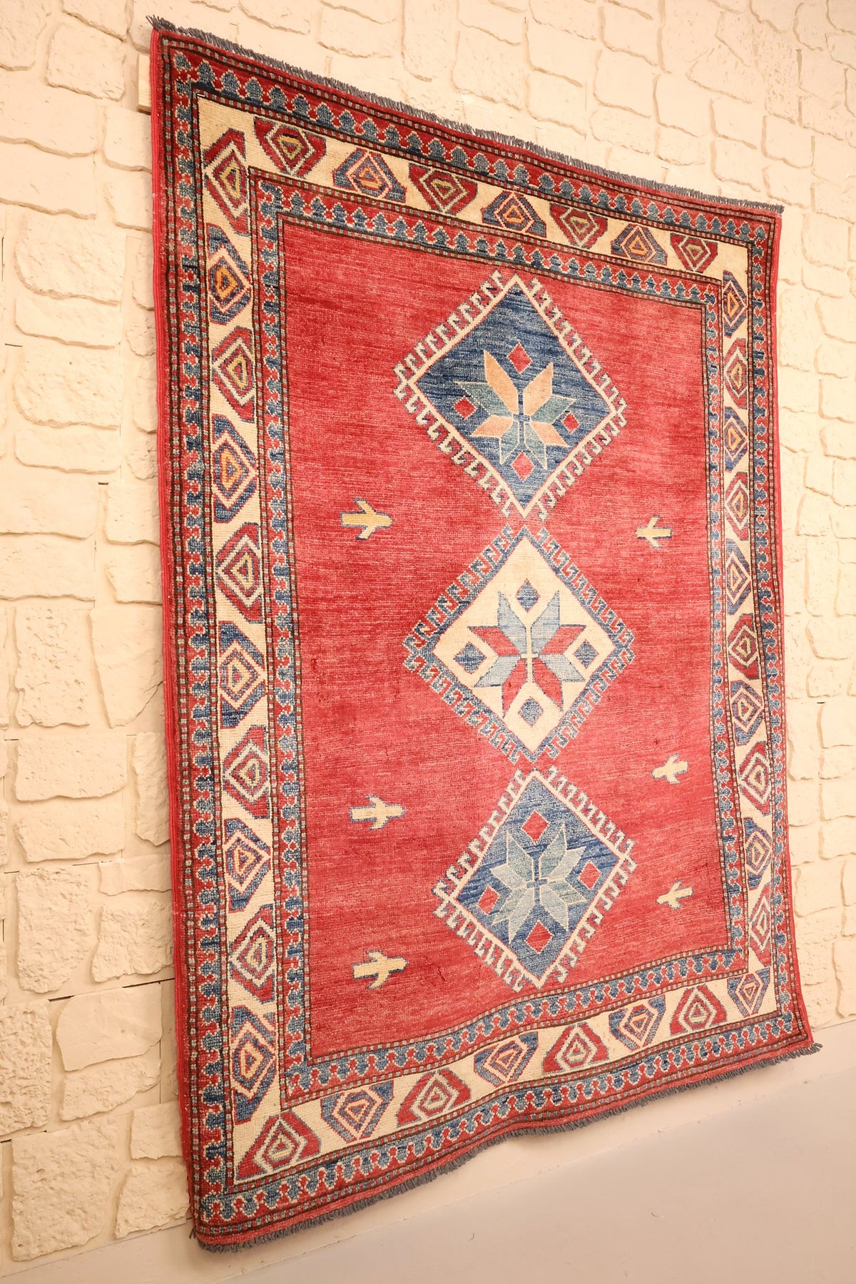 Tapis Kazak rouge et bleu vu de biais, champ uni et bordure beige à losanges