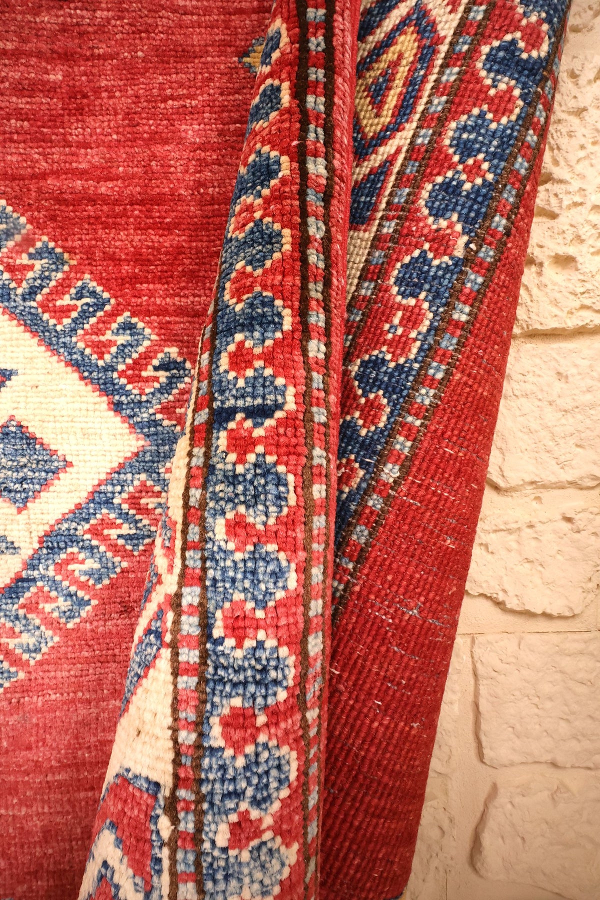 Coin retourné du tapis Kazak noué à la main, envers rouge et bordure bleue
