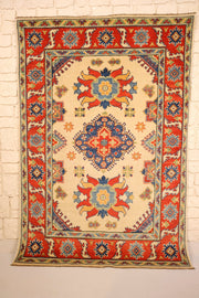 Tapis Kazak beige 178 × 122 cm, vue d'ensemble avec médaillon losange bleu et rosettes rouges
