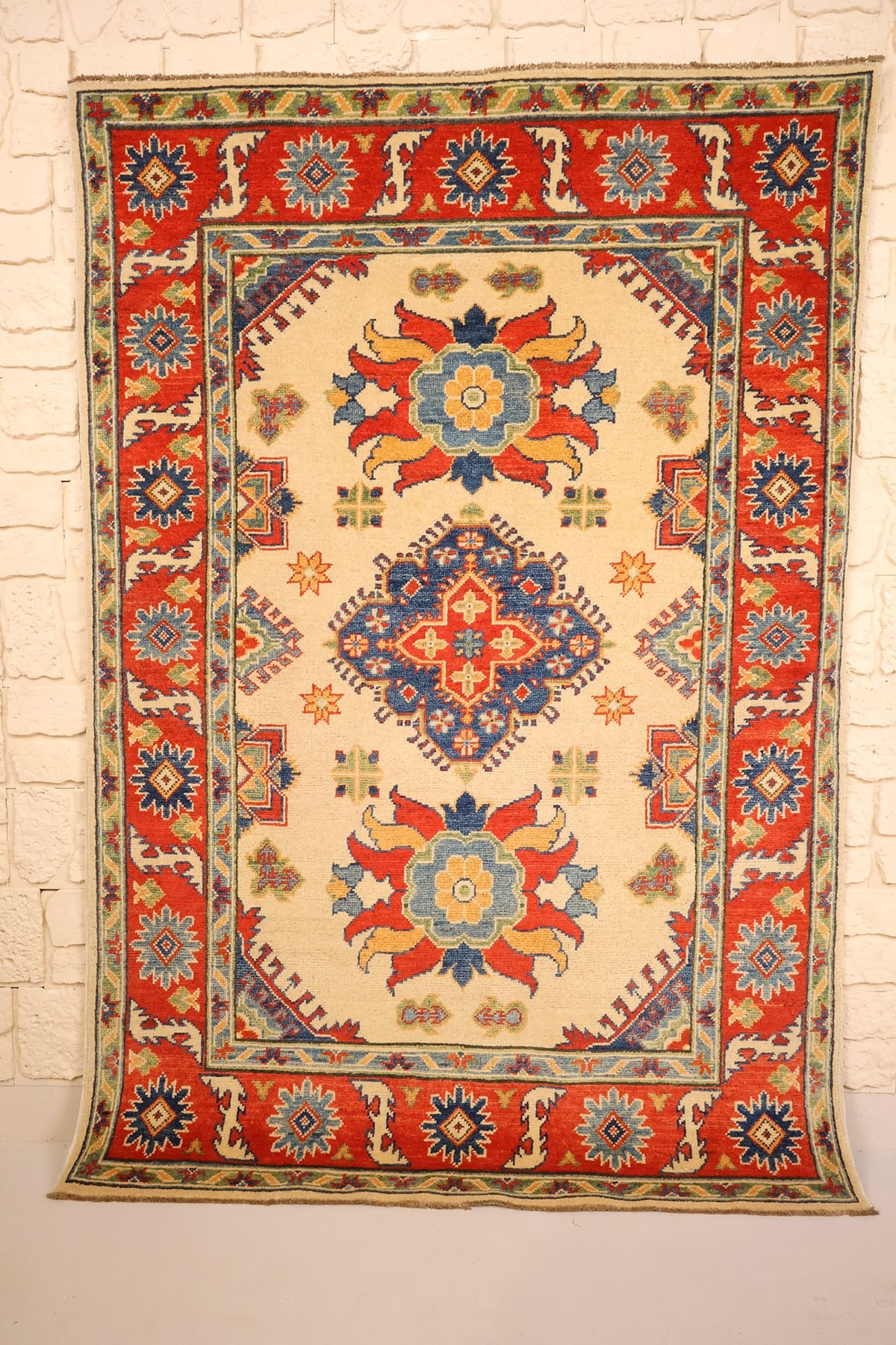 Tapis Kazak beige 178 × 122 cm, vue d'ensemble avec médaillon losange bleu et rosettes rouges