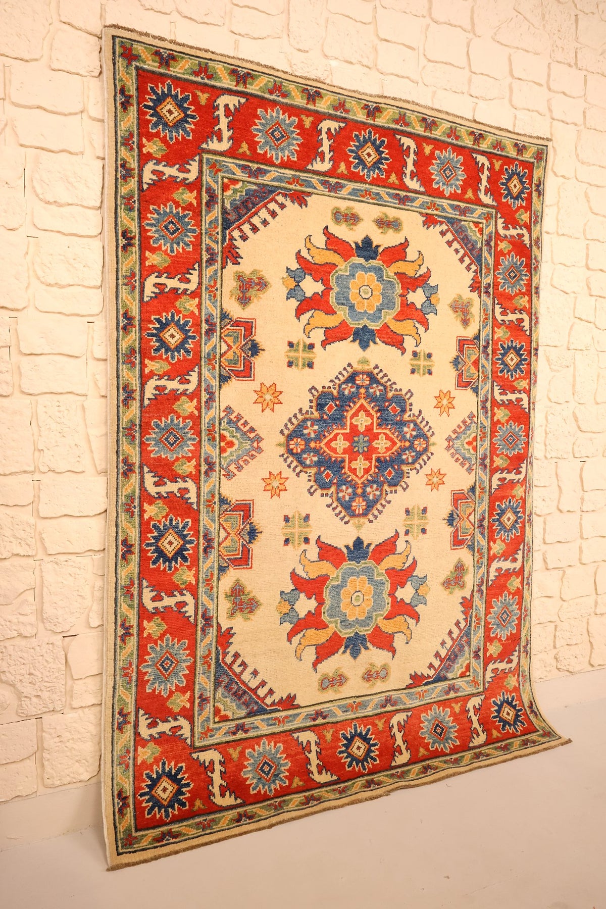 Tapis Kazak beige et rouge en laine, vue de biais montrant le champ ivoire et sa bordure