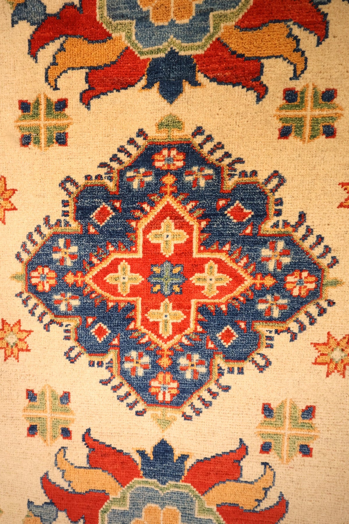 Détail du médaillon central bleu à cœur rouge et des étoiles orange du tapis Kazak