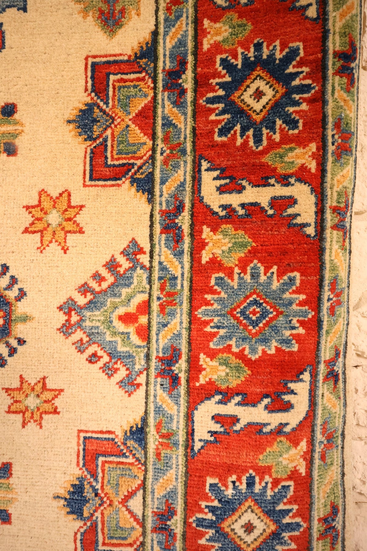 Bordure rouge à étoiles-médaillons bleues et contre-bordures à chevrons du tapis Kazak